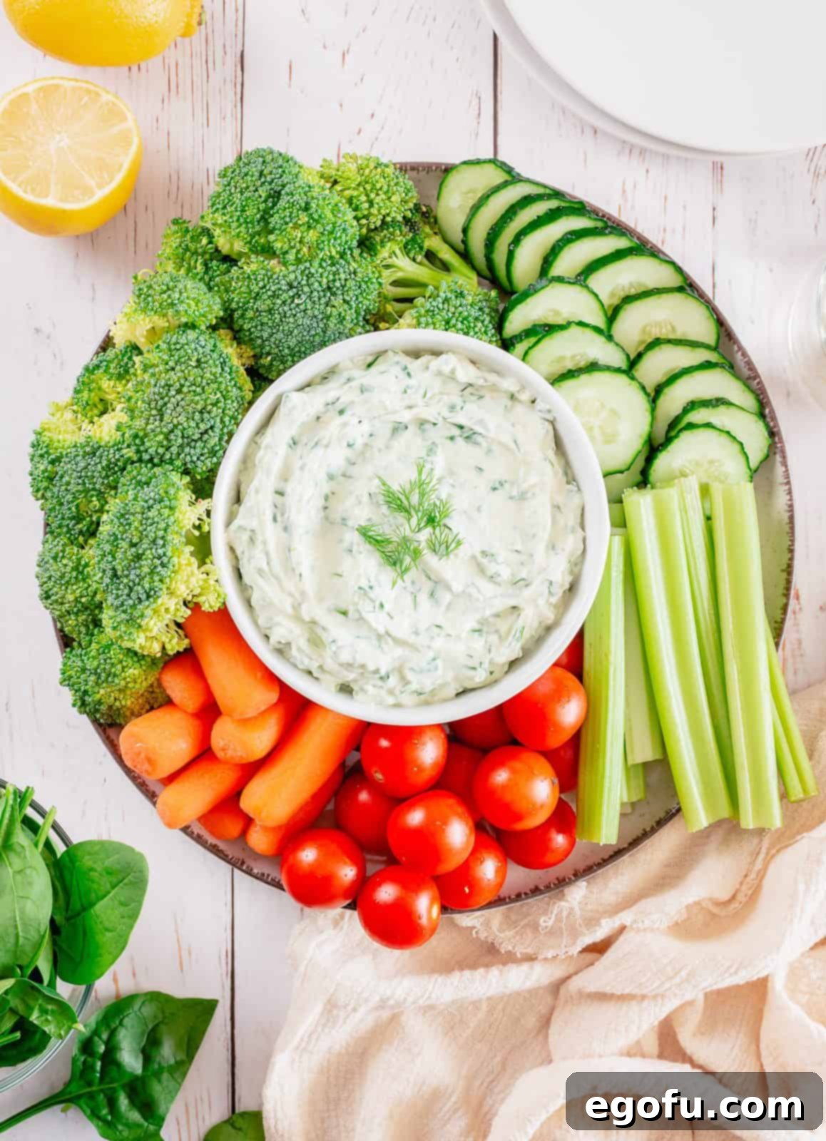 Chilled Garden Spinach Dip 6 An inviting overhead shot of the Classic Spinach Dip, generously garnished with a sprig of fresh dill, beautifully presented in a rustic bowl amidst an artful arrangement of colorful fresh vegetables and various crunchy dippers.