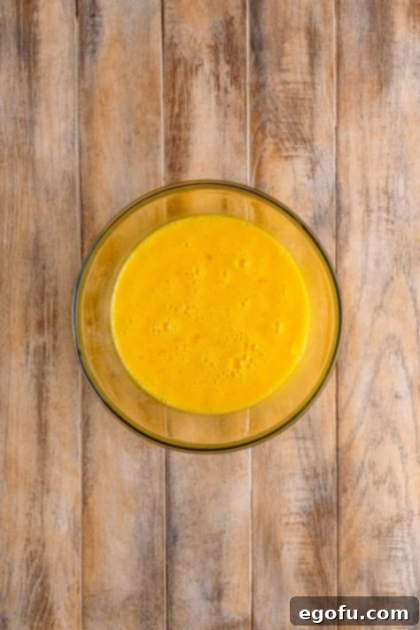 Starbucks' Bite-Sized Egg Delights 11 Eighteen eggs shown vigorously whisked together in a clear mixing bowl, creating a smooth, pale yellow mixture.