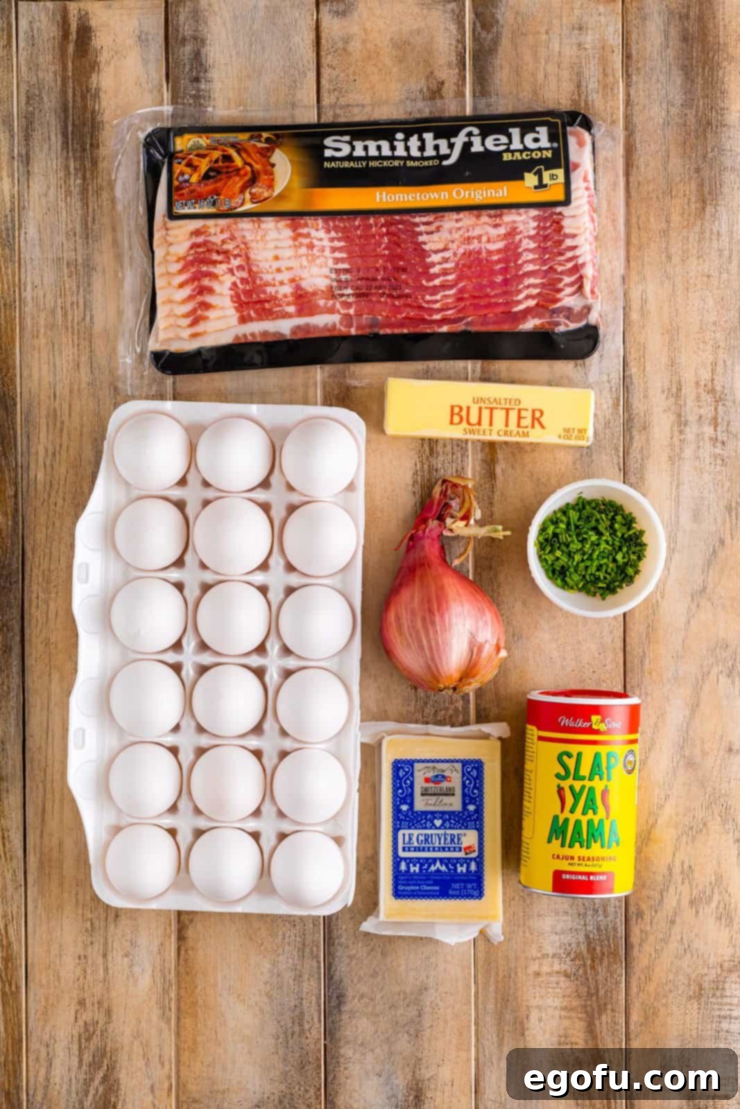 Starbucks' Bite-Sized Egg Delights 5 A thoughtfully arranged collection of fresh ingredients on a clean countertop, including a bowl of raw large eggs, crispy strips of cooked bacon, finely minced shallots, a stick of unsalted butter, vibrant fresh chives, a substantial block of Gruyere cheese, and a small container of Creole seasoning.