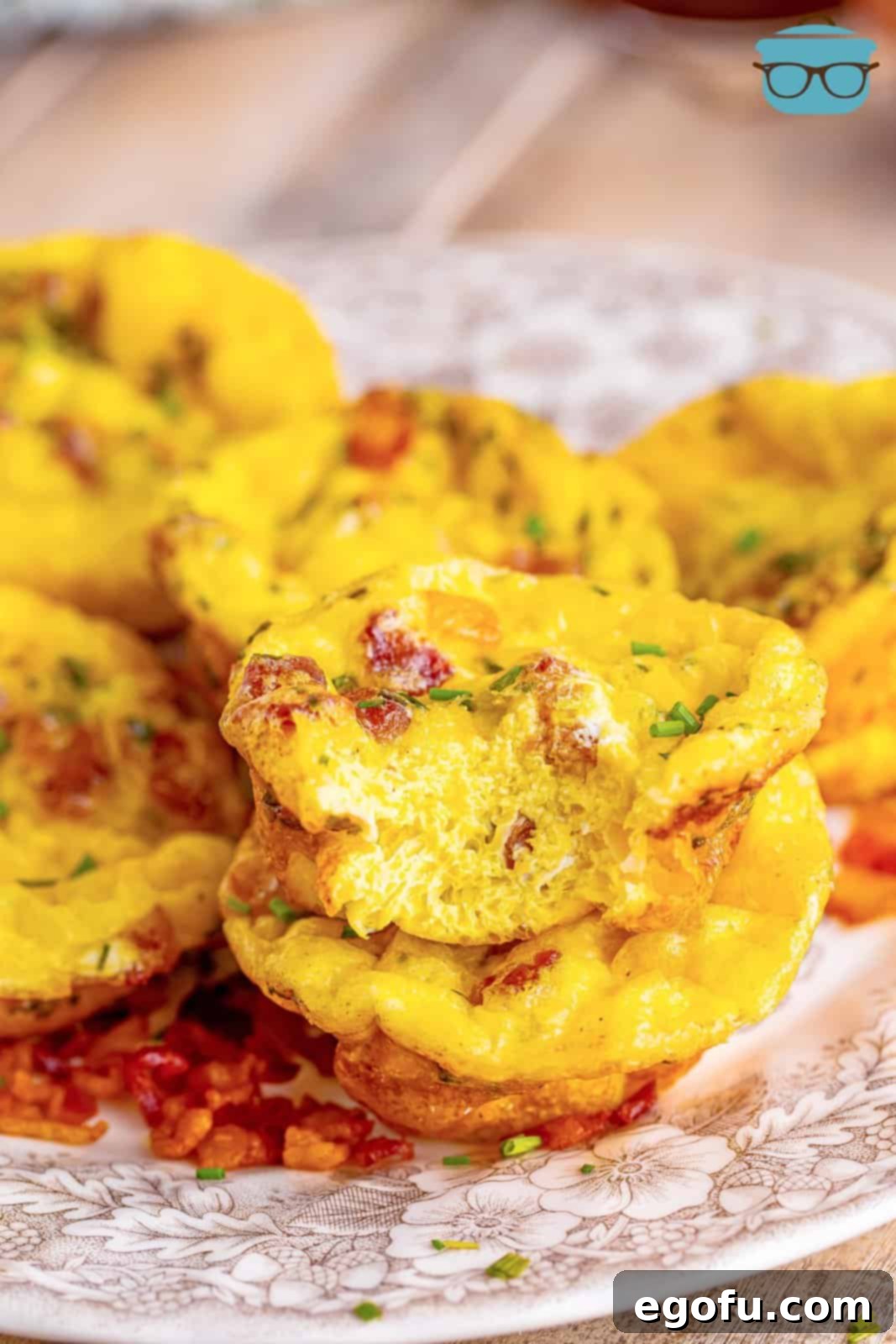 Starbucks' Bite-Sized Egg Delights 9 A single, perfectly baked egg bite is displayed with a portion removed, revealing its fluffy interior, and neatly stacked among several other pristine egg bites on a charming brown and white floral plate, highlighting their appetizing texture and inviting presentation.