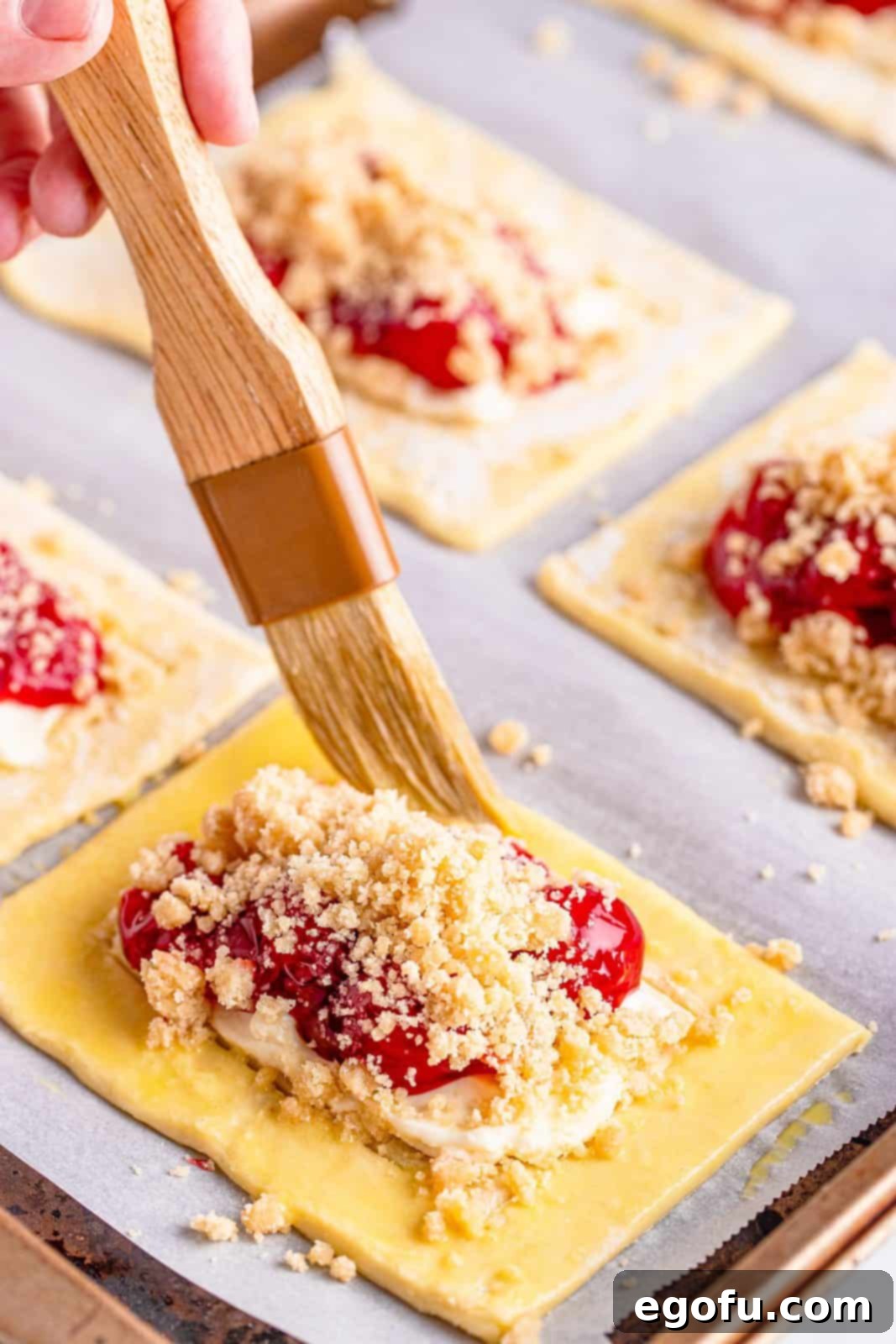 Buttery Cherry Crumble Danishes 12 Pastry brush brushing egg wash on edges of puff pastry.