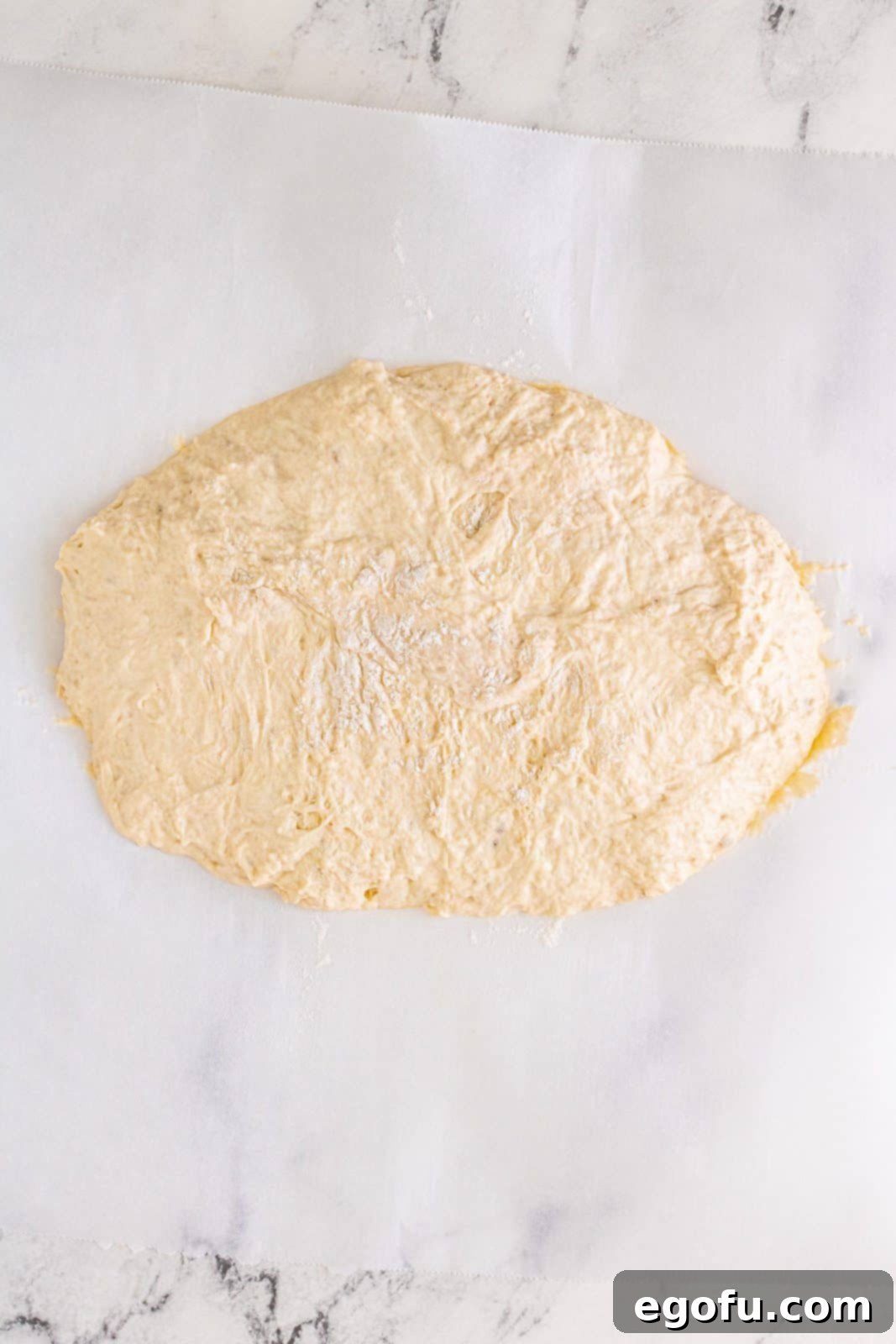 No-knead dough gently placed on parchment paper, lightly dusted with flour and shaped into a round.