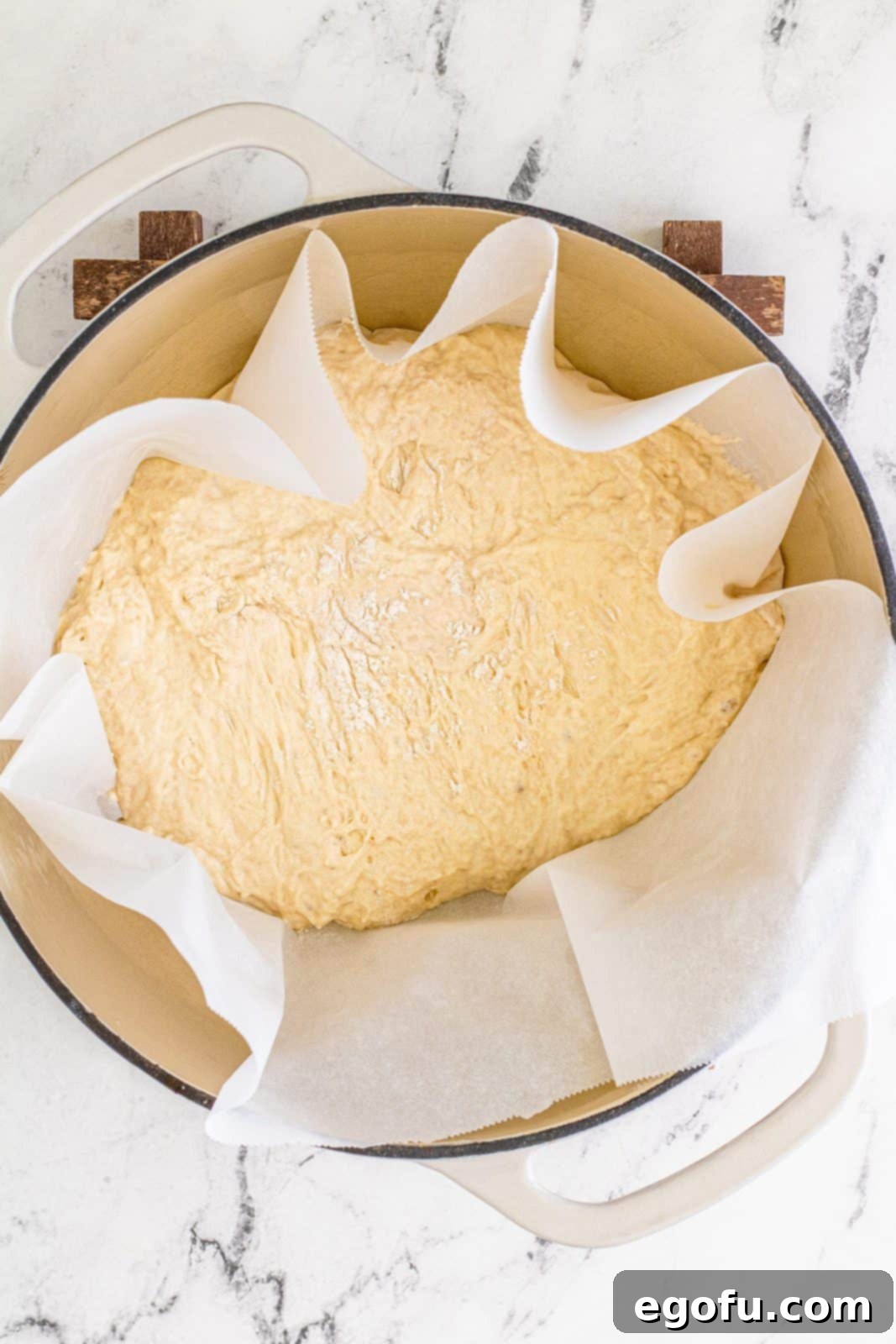 Parchment paper with dough carefully lowered into a hot Dutch oven, ready for baking.