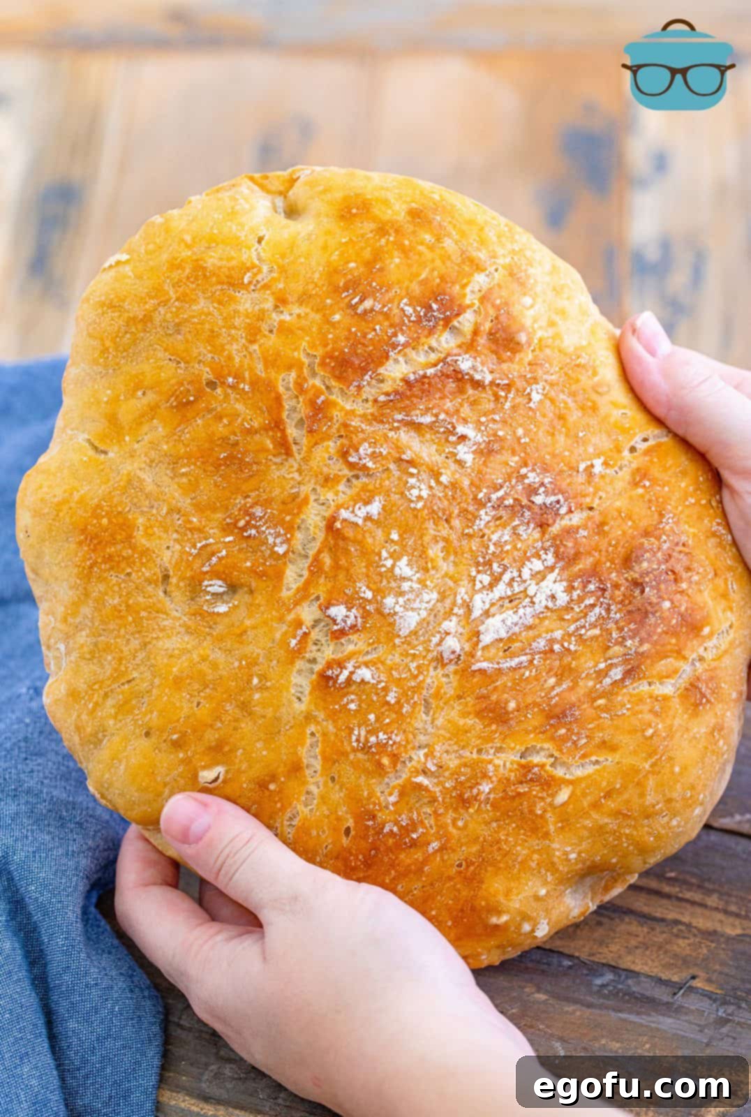 Hands holding a freshly baked loaf of No-Knead Dutch Oven Bread, showcasing its perfectly golden and crusty exterior.