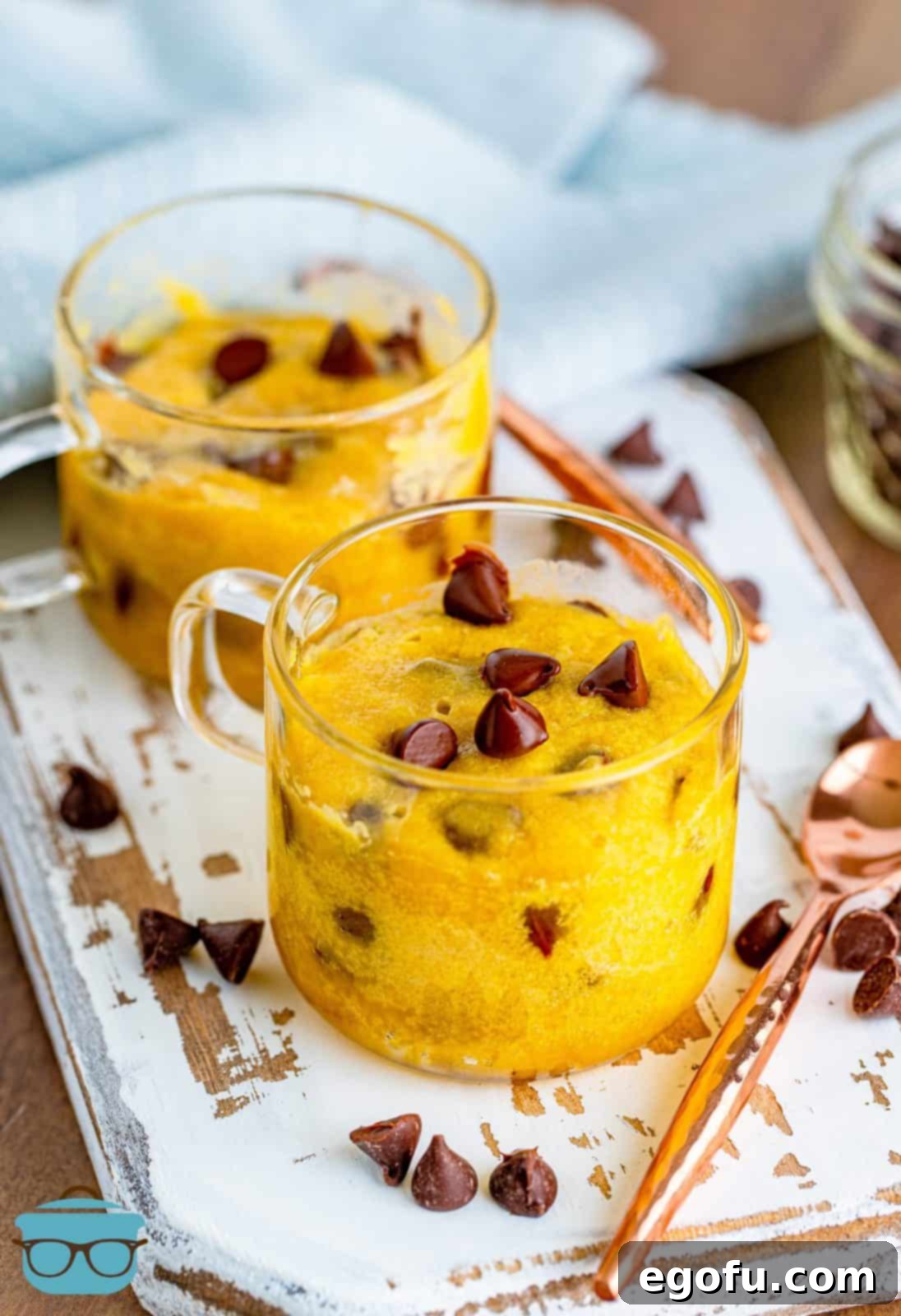 two chocolate chip cookies in a mug shown on a white board.