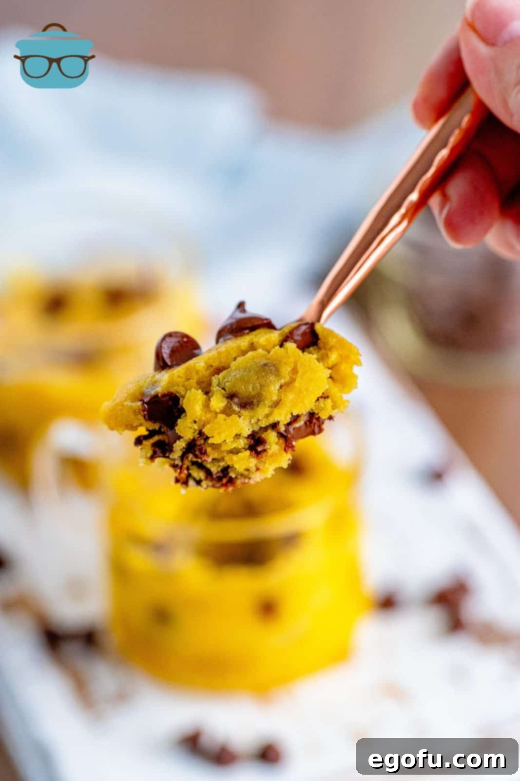 a rose gold spoon holding a serving of chocolate chip cookie over a mug.