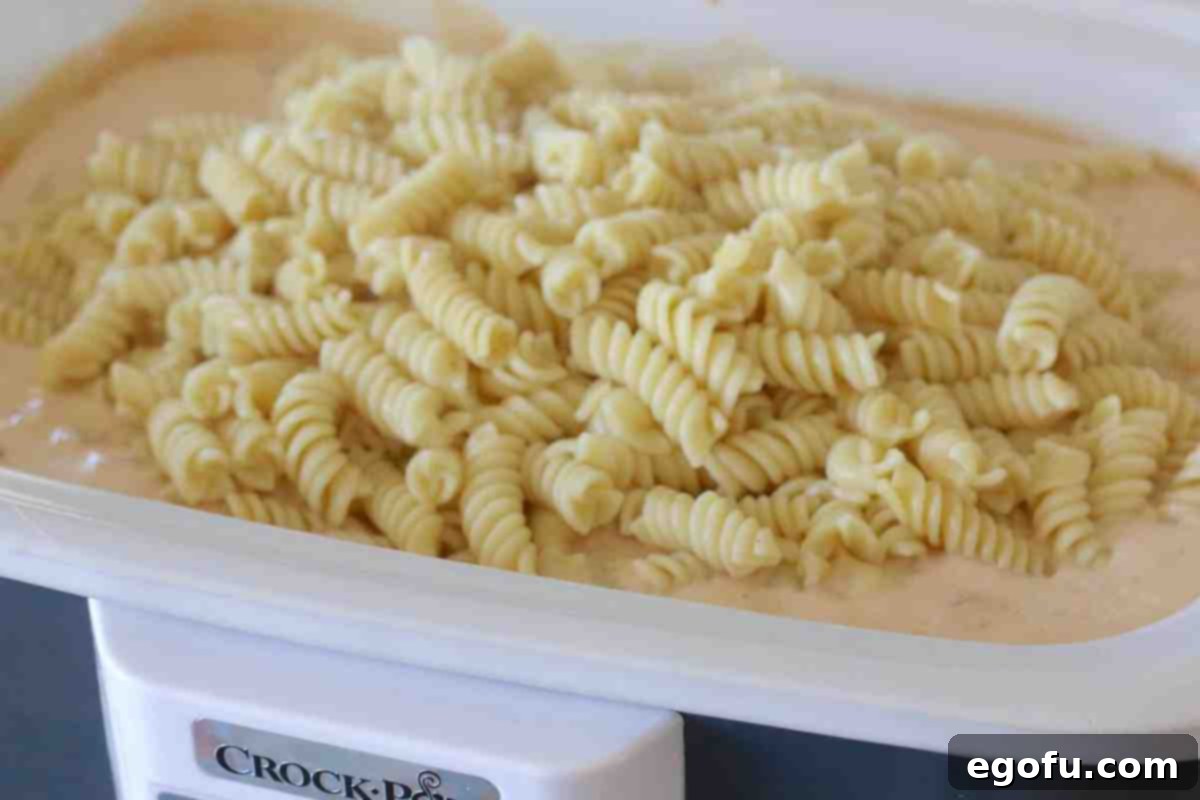 Cooked rotini pasta added to the slow cooker with the chicken and sauce mixture.