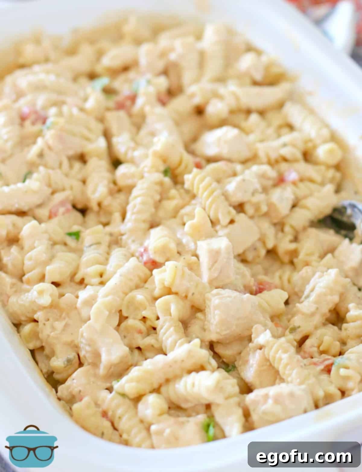 Fully cooked and combined Slow Cooker Chicken Ranch Pasta recipe shown in casserole slow cooker with a serving spoon, ready to be dished out.