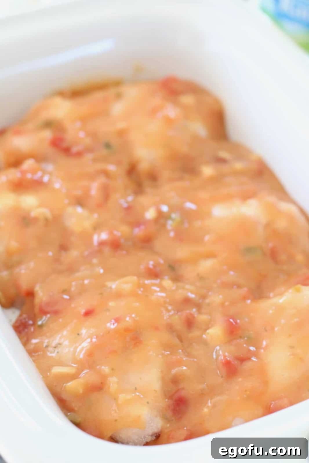 Salsa mixture being poured over frozen chicken breasts in a white casserole crock pot.