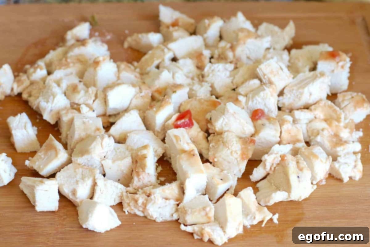 Cooked chicken cut into chunks on a wooden cutting board, ready to be added back to the slow cooker.