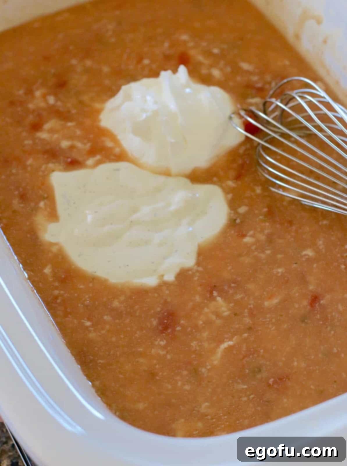 Sour cream and ranch dressing being whisked into the salsa mixture at the bottom of a casserole slow cooker.