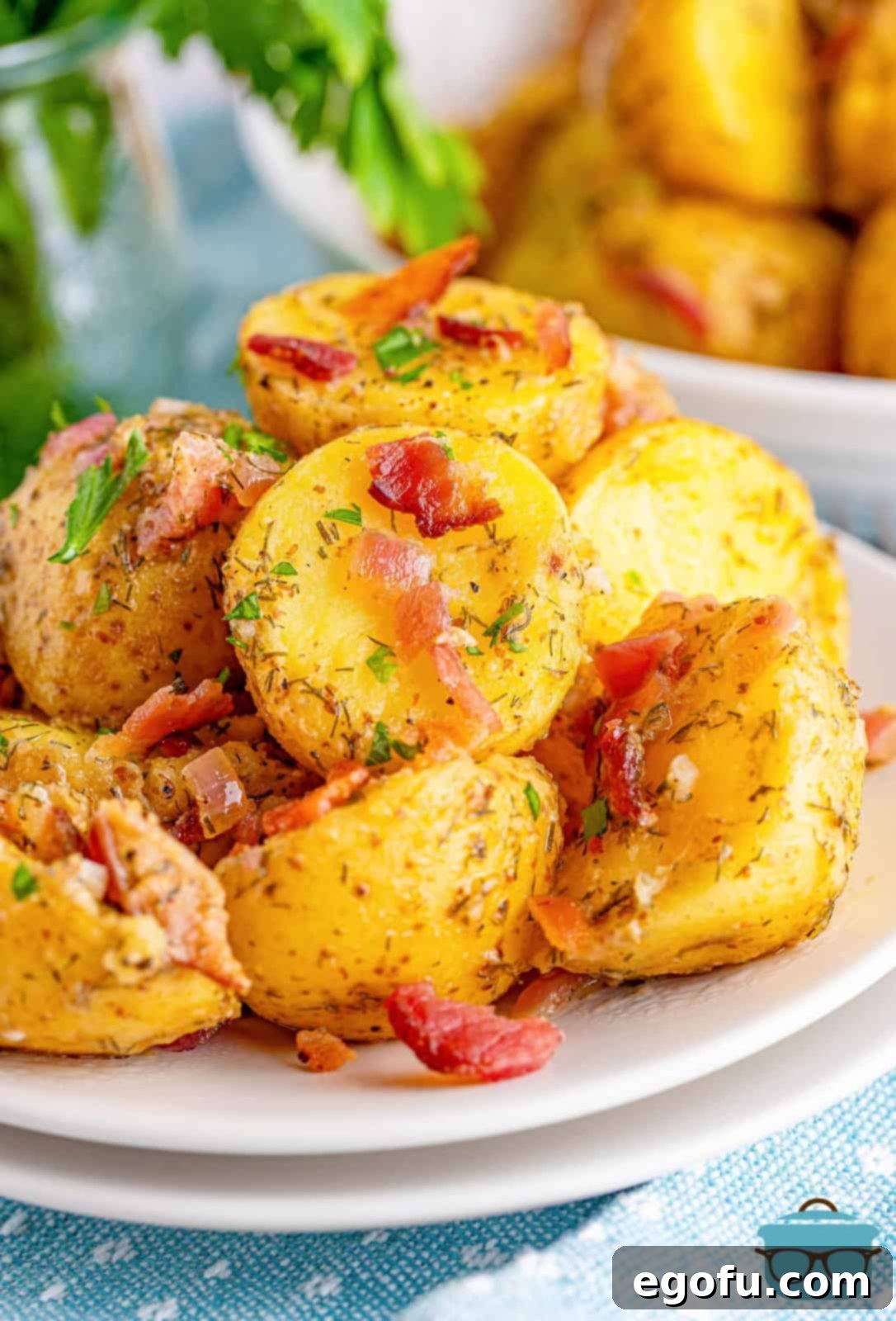 A serving of warm bacon potato salad shown on two small white stacked plates, garnished with fresh parsley.