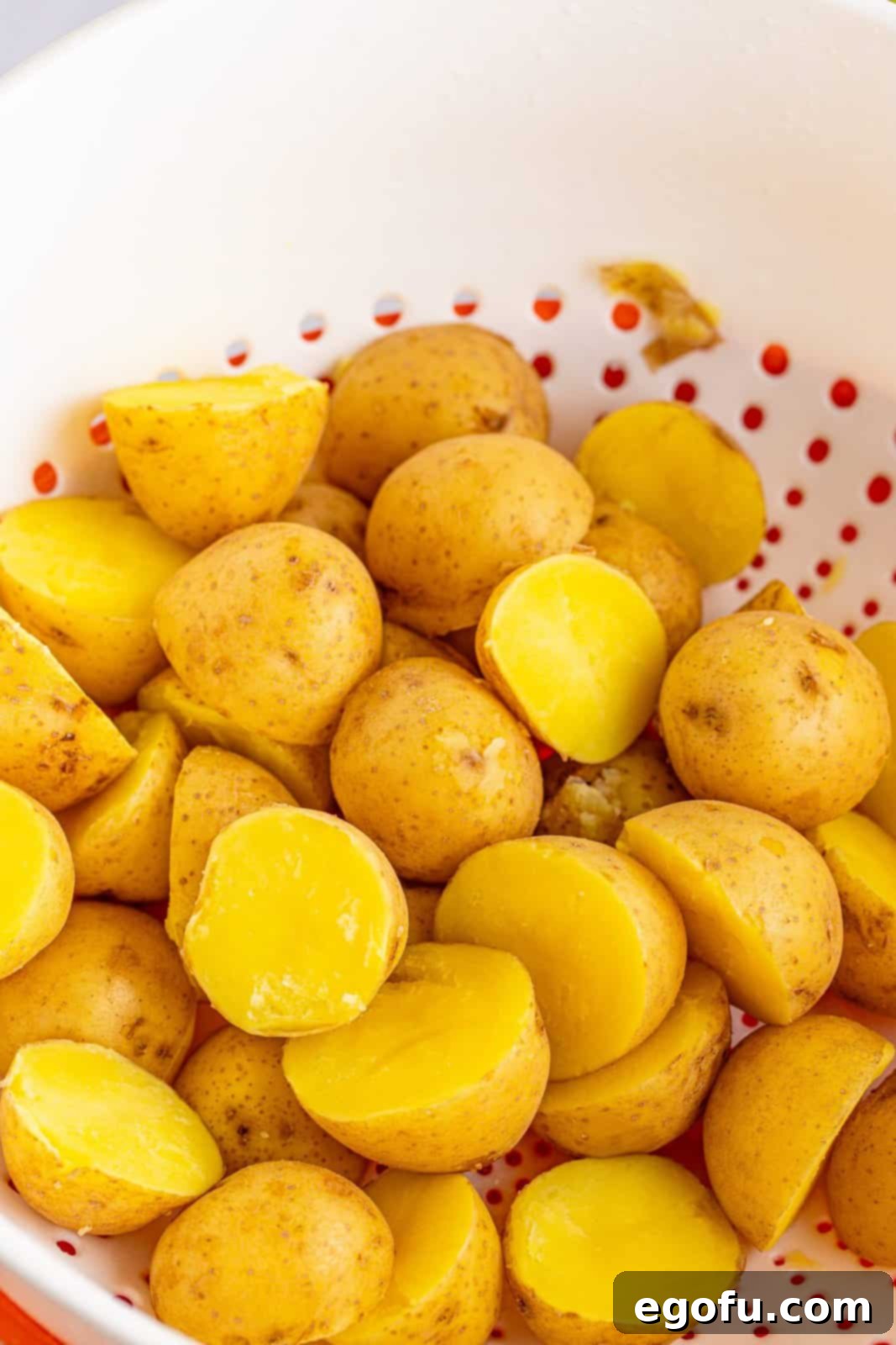 Cooked and drained baby gold potatoes resting in a white colander, ready for the next step of the recipe.