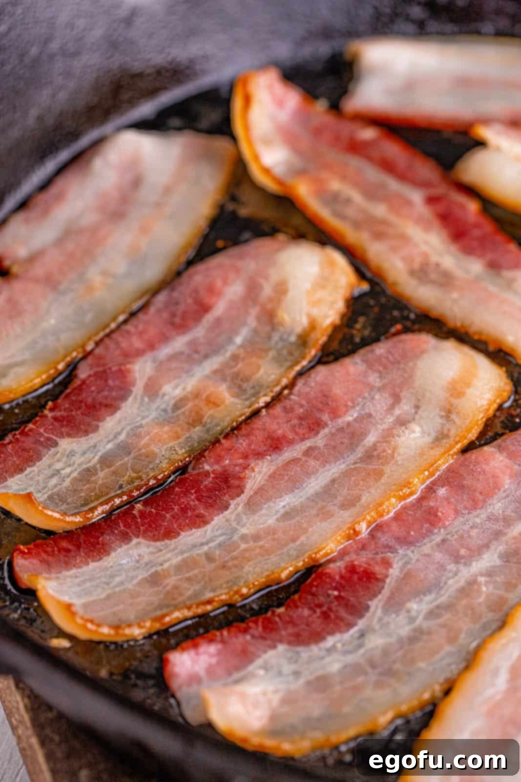 Crispy bacon pieces cooking in a rustic cast iron frying pan, rendering flavorful grease.