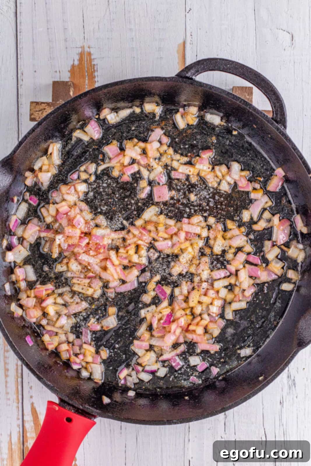 Finely diced red onion gently cooking in rich bacon grease in a cast iron skillet, softening to release its sweet flavor.