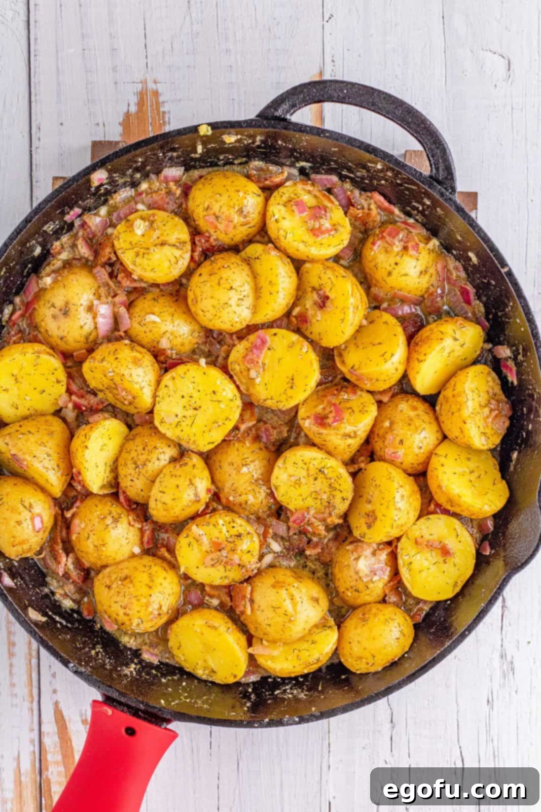 Cooked potatoes, prepared vinaigrette, and crumbled bacon mixed together in a large pan, warming up to meld flavors.