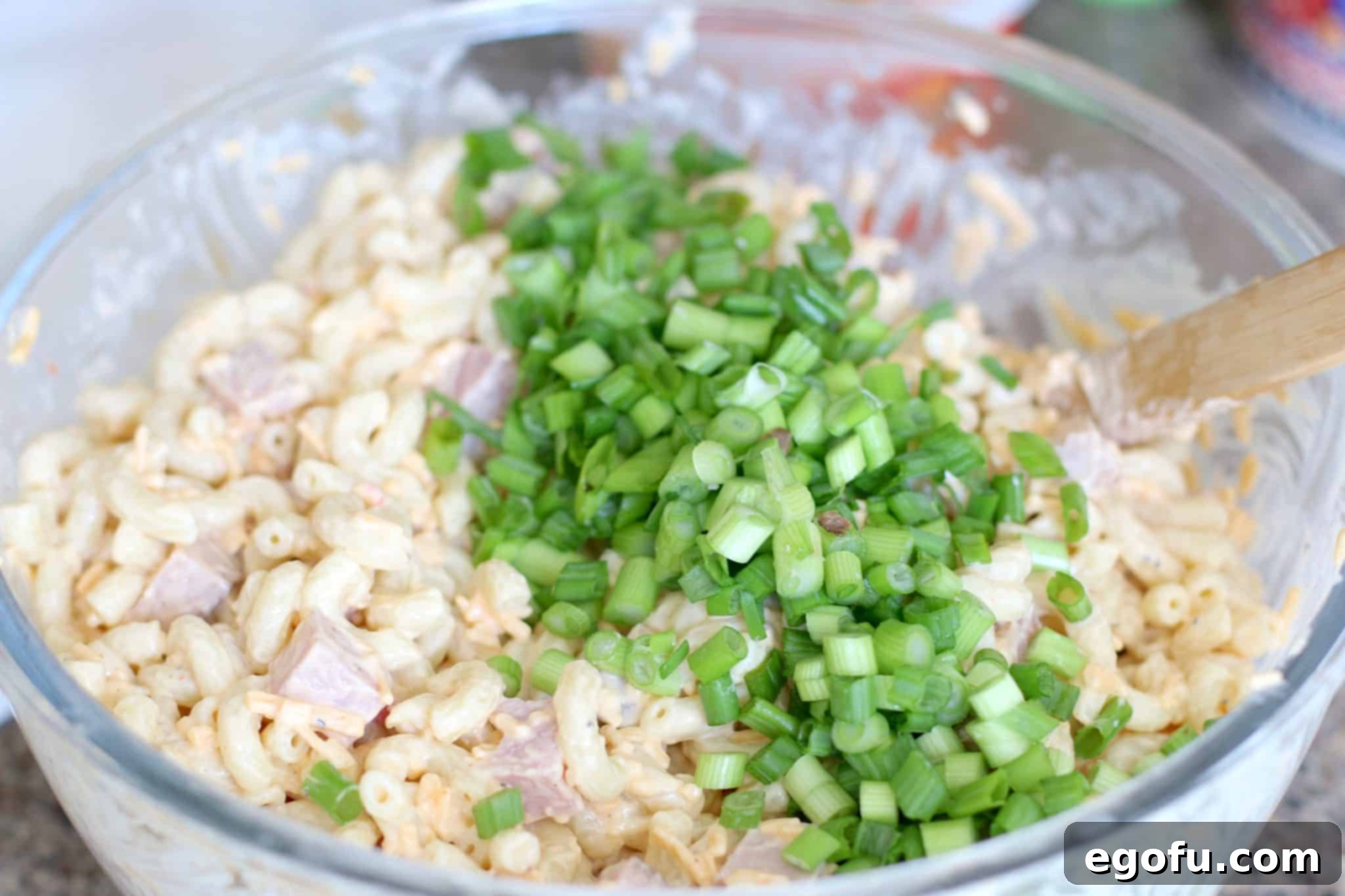 Homestyle Pimiento Macaroni Salad 10 green onion, ham, macaroni salad with mayonnaise, salt and pepper in a large bowl stirred with a wooden spoon.