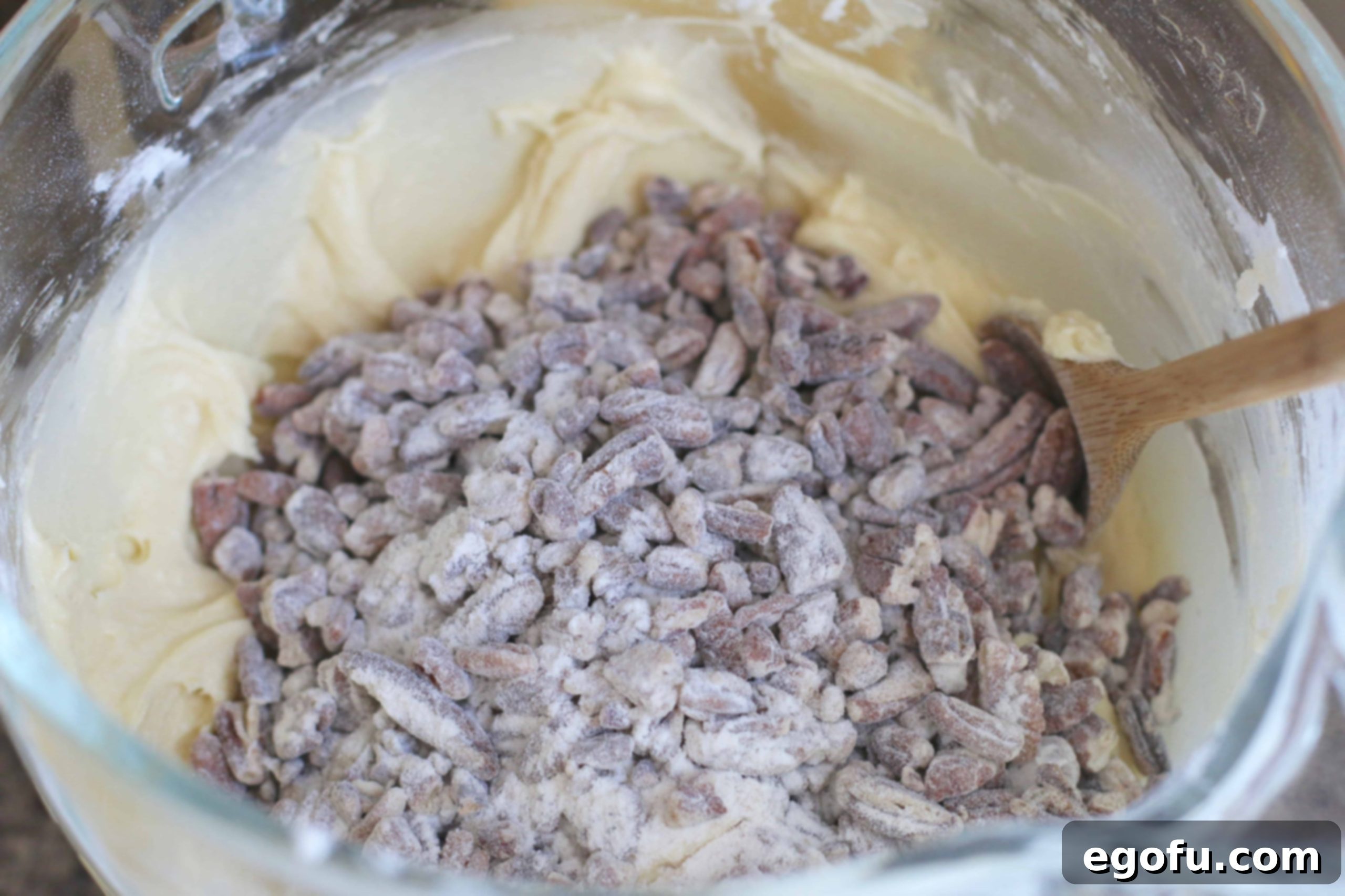 Heirloom Southern Pecan Pound Cake 11 Flour-coated chopped pecans being hand-stirred into the thick, luscious pound cake batter in a large bowl, ensuring even distribution of nuts.