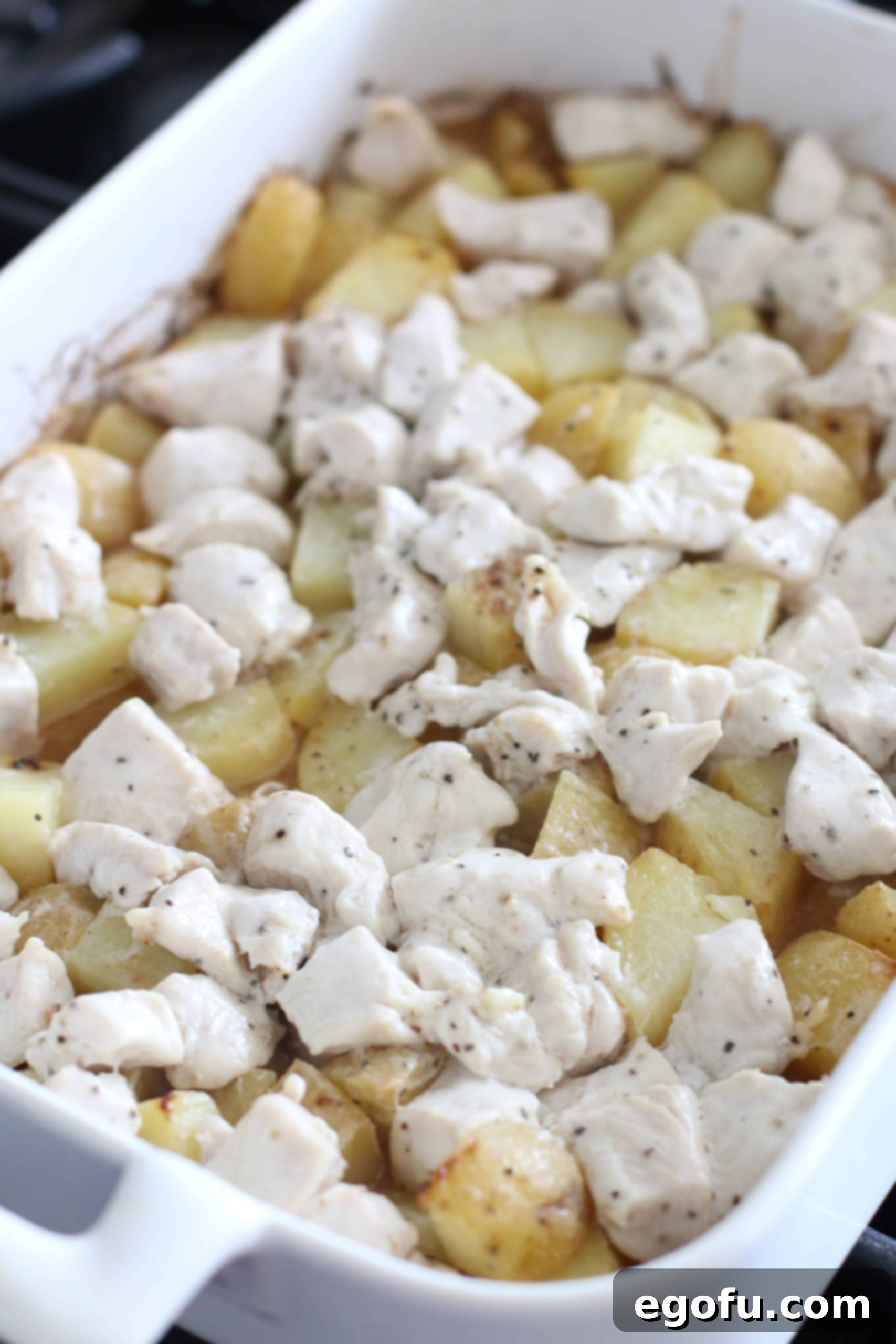 Cooked baked chicken and potatoes in a white baking dish, fresh out of the oven.