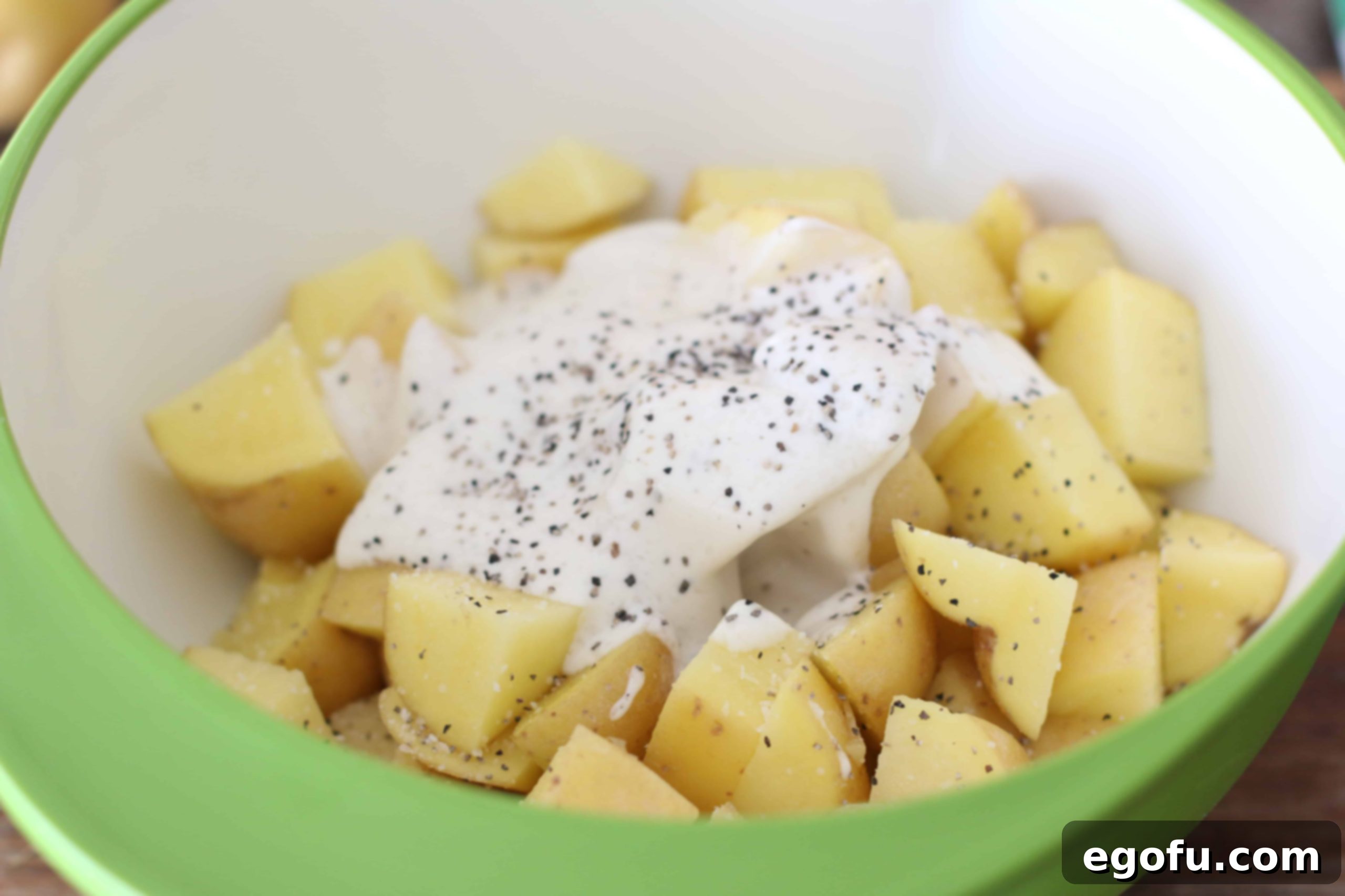 Diced potatoes being mixed with ranch dressing, salt, and pepper in a large bowl.