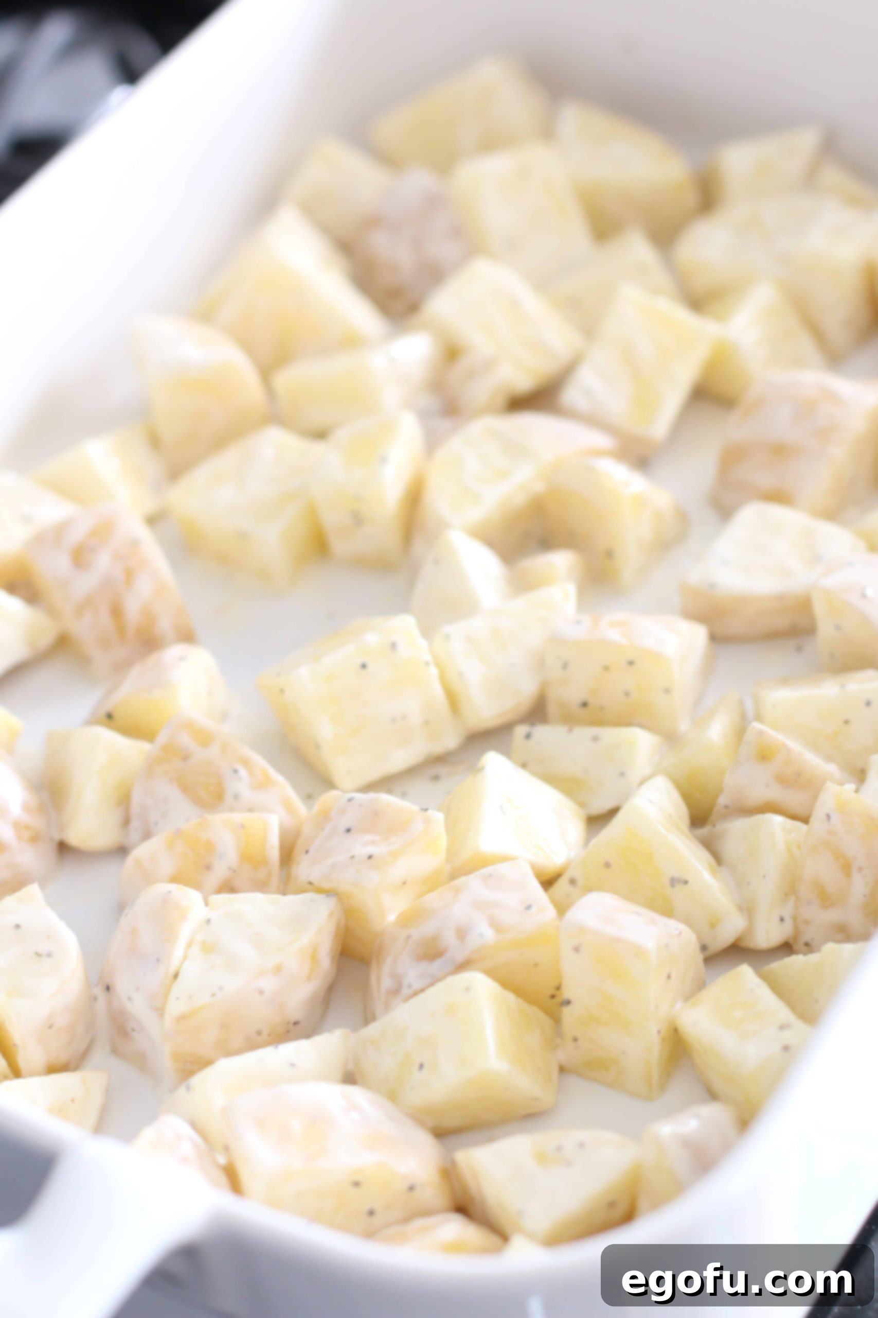 Ranch-coated potatoes spread evenly in the bottom of a white casserole dish, ready for baking.