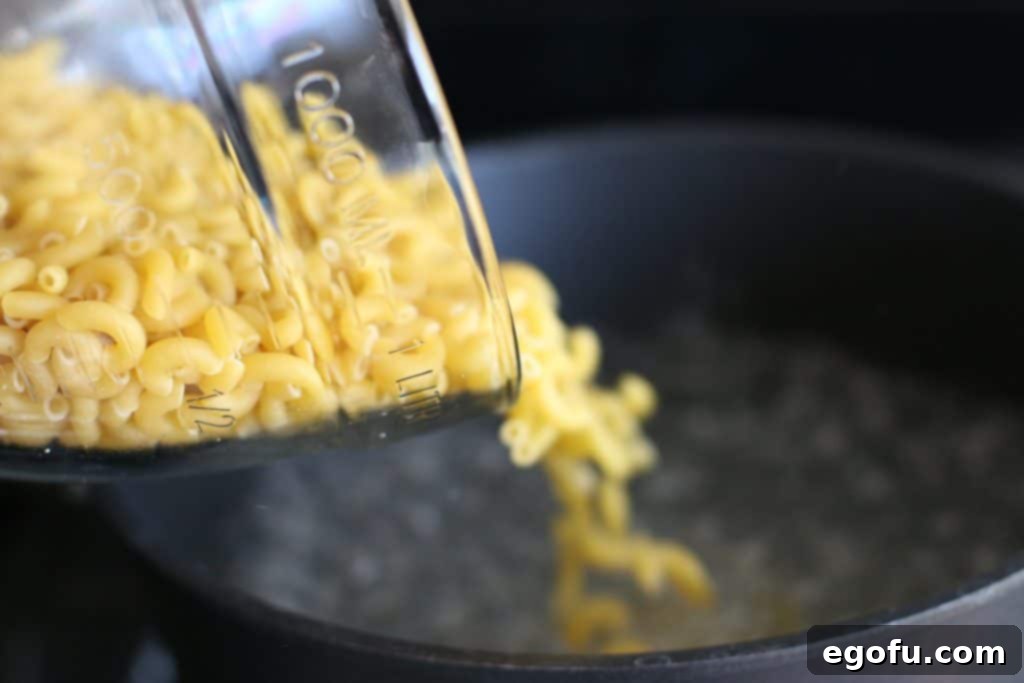Elbow macaroni noodles being poured into a large pot of boiling water, ready to be cooked to al dente perfection.