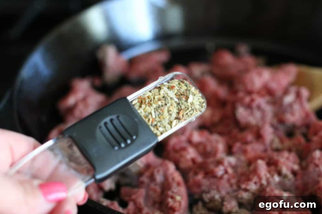 Italian seasoning being sprinkled over cooking ground beef in a skillet, filling the kitchen with fragrant aromas.
