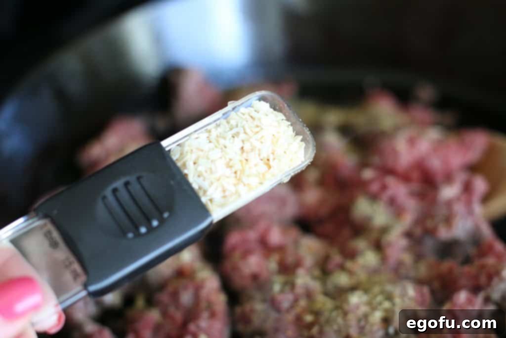 Dried onion flakes being added to the sizzling ground beef in a skillet, ready to enhance the savory flavor.