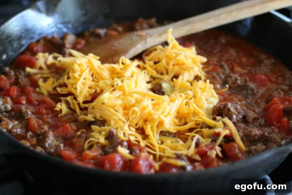 Shredded cheddar cheese melting into the rich tomato and ground beef mixture in the skillet, promising a creamy and delicious sauce.