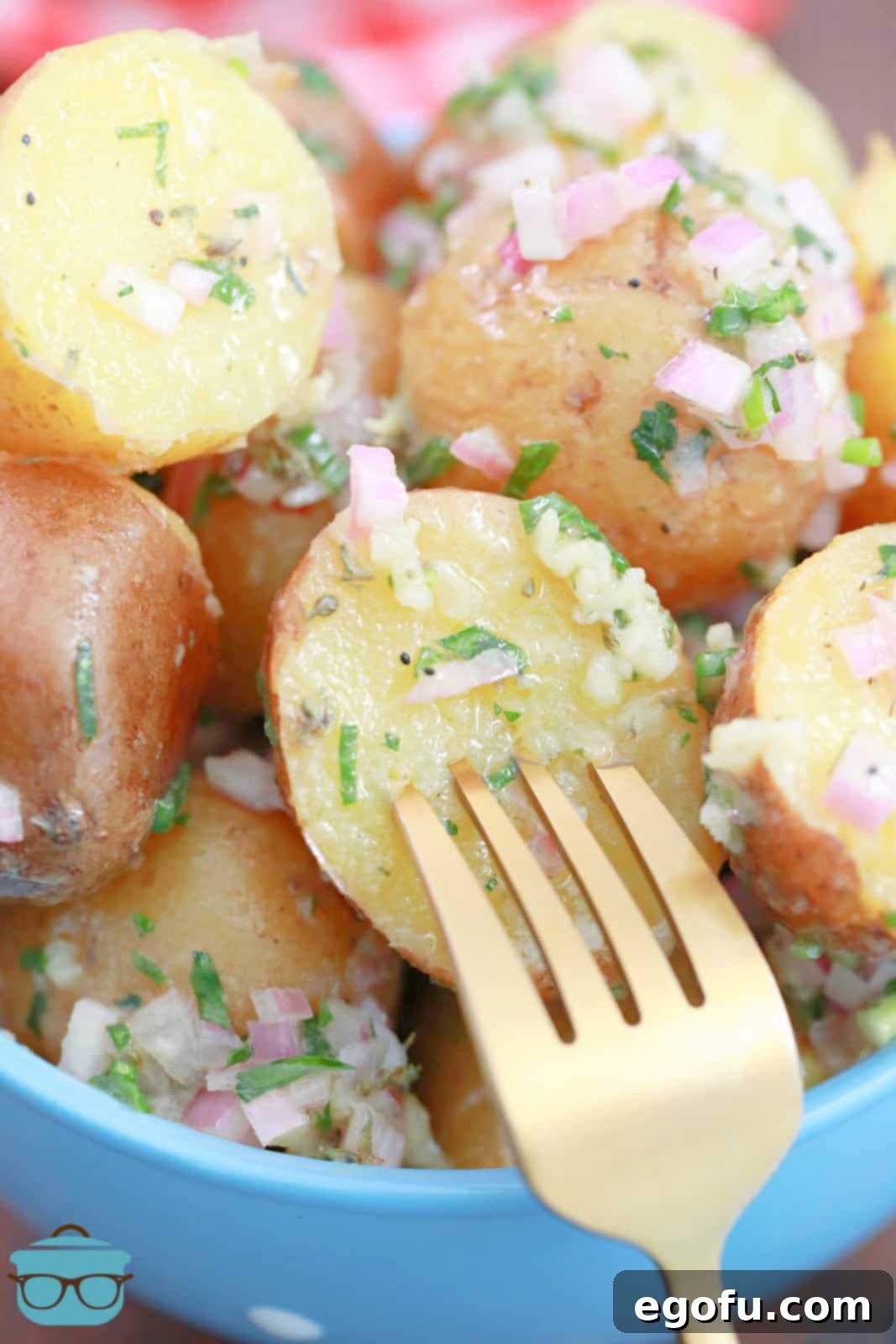 A fork piercing a potato piece coated in a vibrant fresh herb vinaigrette, showcasing the French Potato Salad.