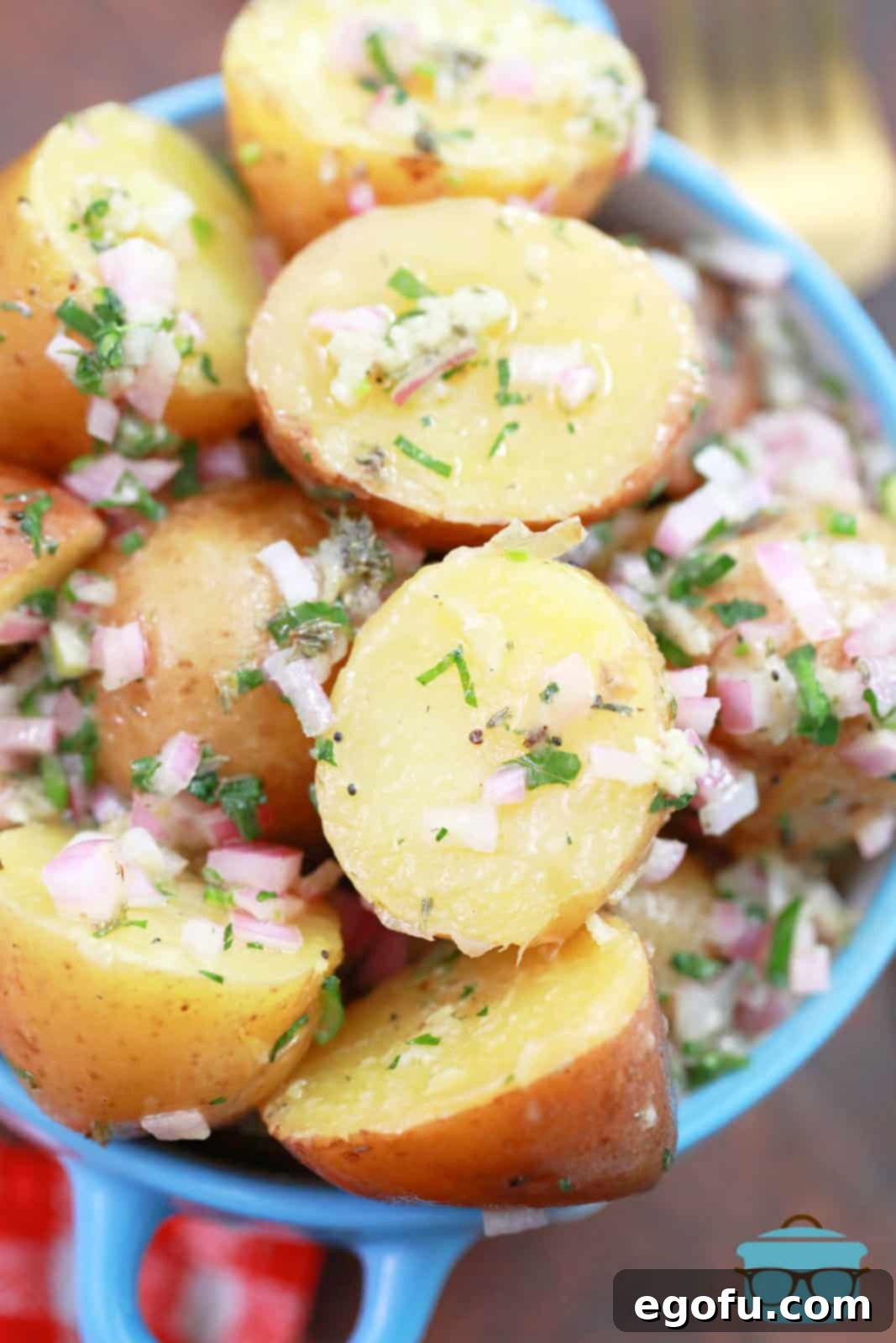 A small blue bowl with handles filled with perfectly dressed French Potato Salad, a fork resting beside it.