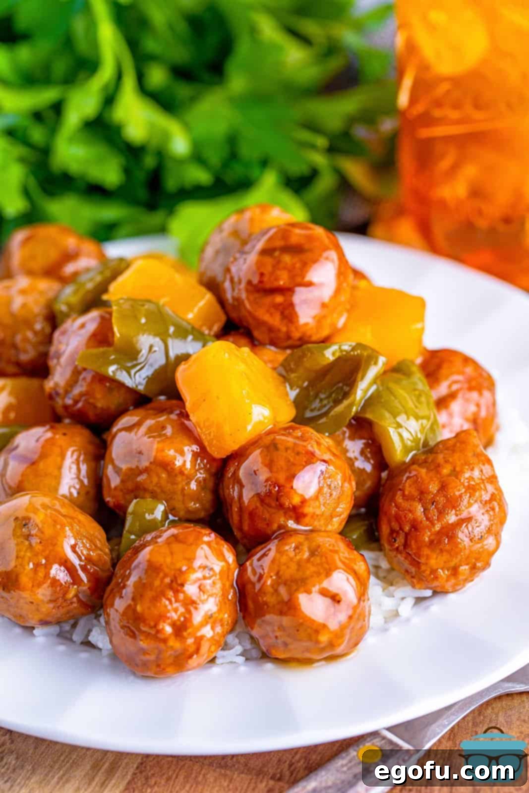 Sticky Sweet & Sour Crockpot Meatballs 2 Sweet and sour meatballs shown on white rice on a white plate with a glass of iced tea in the background.