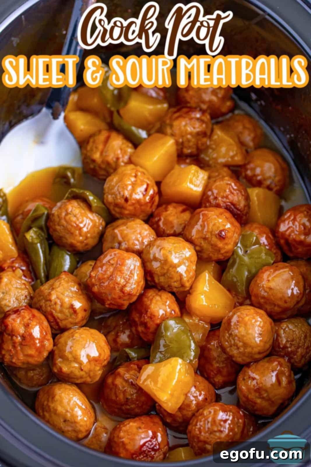 Sticky Sweet & Sour Crockpot Meatballs 4 Fully cooked sweet and sour meatballs in a black oval slow cooker with a silver spoon inserted into the meatballs.