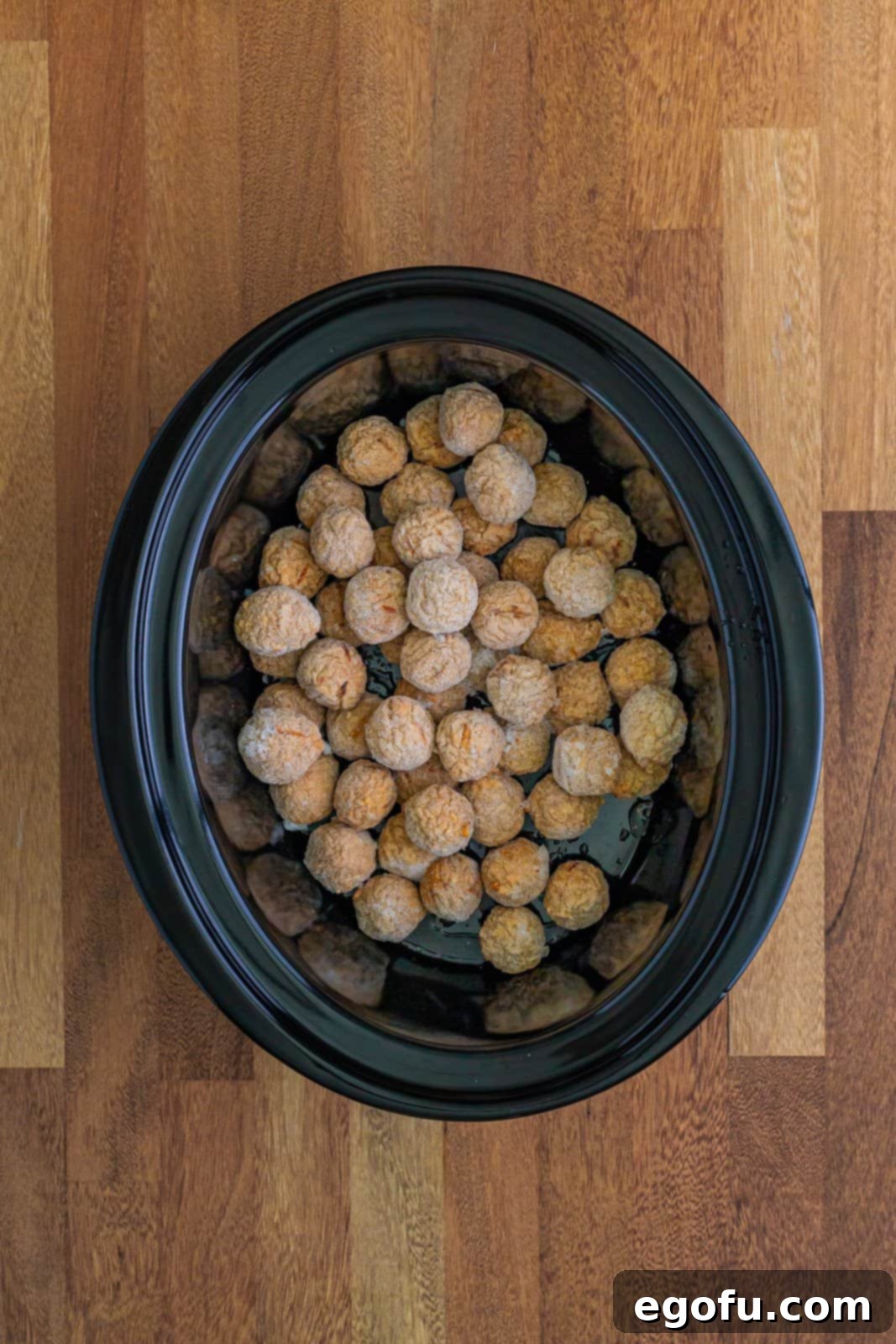 Sticky Sweet & Sour Crockpot Meatballs 7 Frozen meatballs shown at the bottom of an oval black slow cooker.