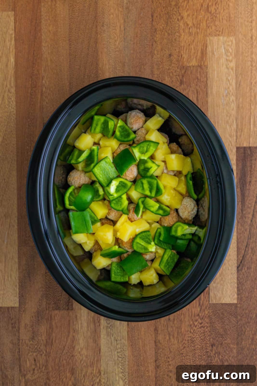 Sticky Sweet & Sour Crockpot Meatballs 8 Chopped green peppers and pineapple chunks shown on top of the frozen meatballs in a slow cooker.