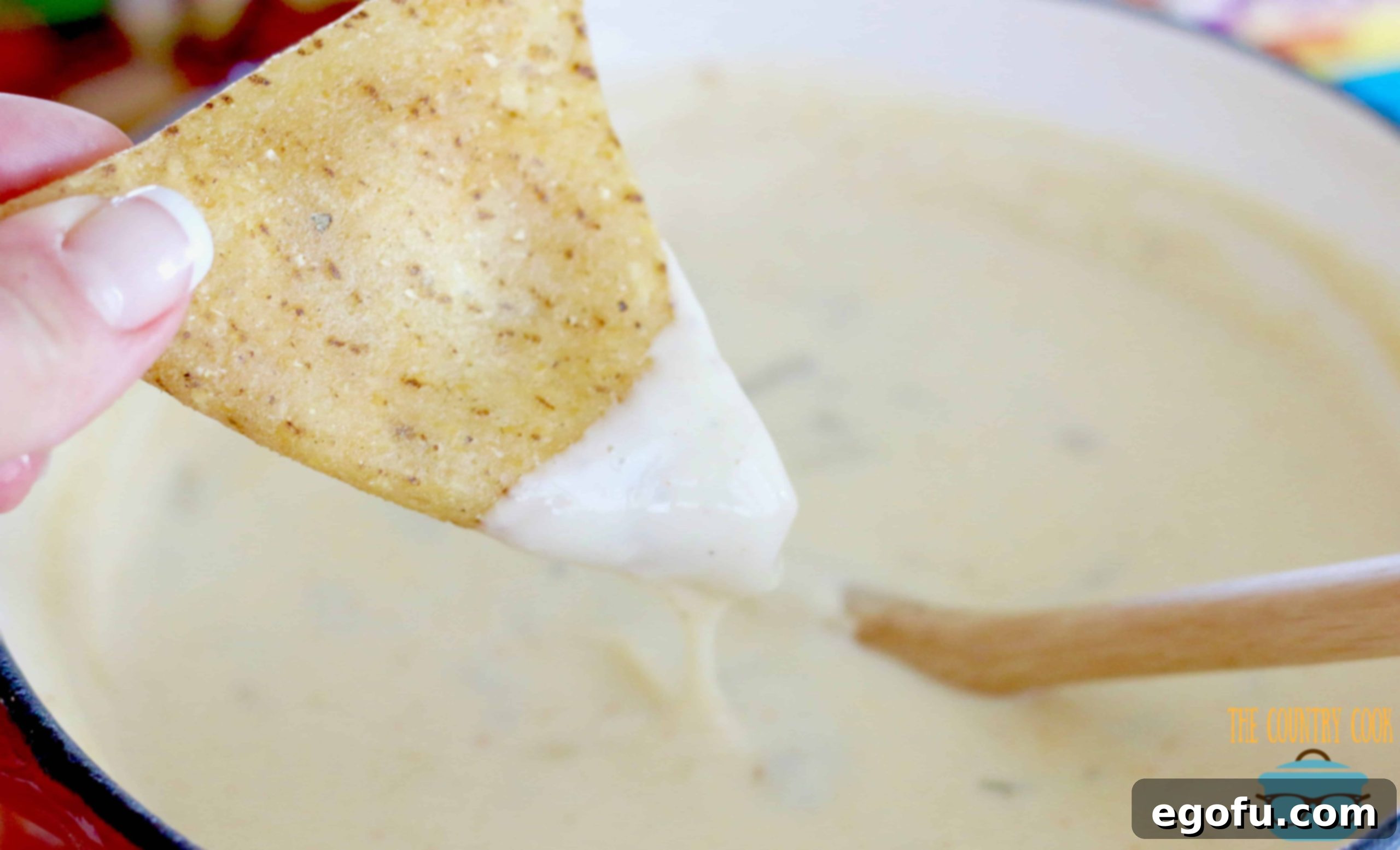 a hand holding a mini taco over a bowl of white queso dip. 