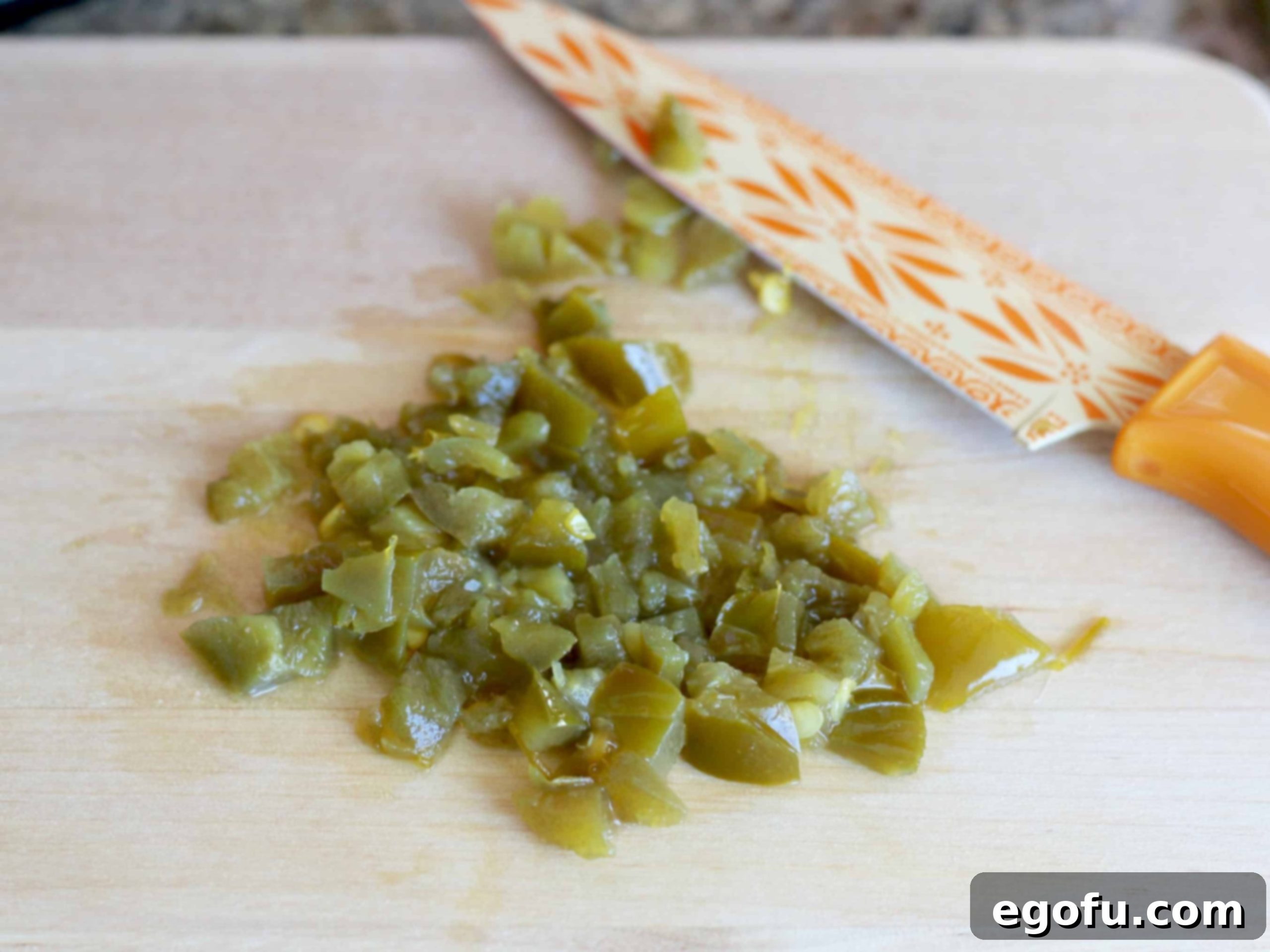 diced jalapeños on a wood cutting board with a knife. 