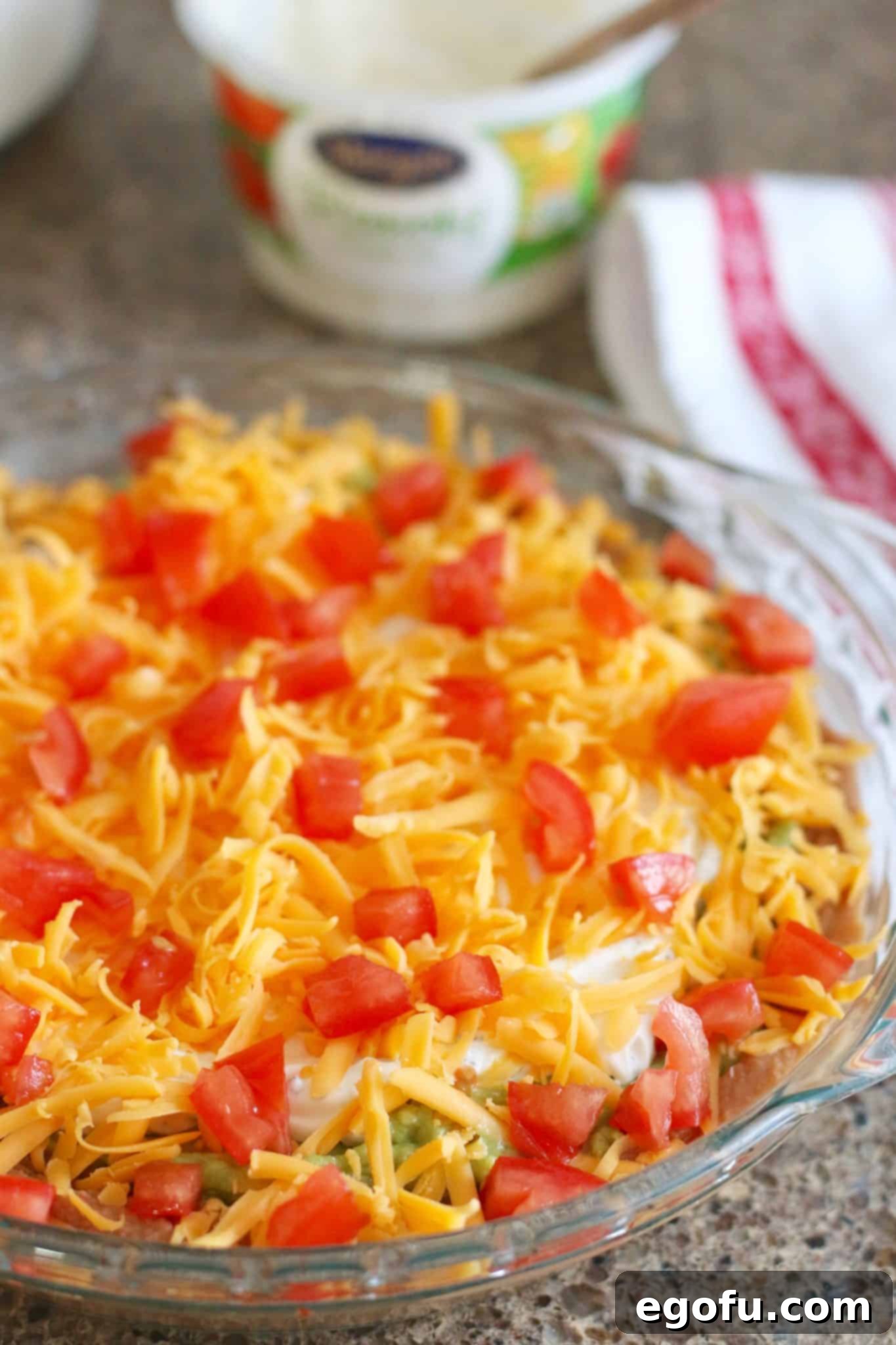 mexican layer dip topped with shredded cheese and diced tomatoes