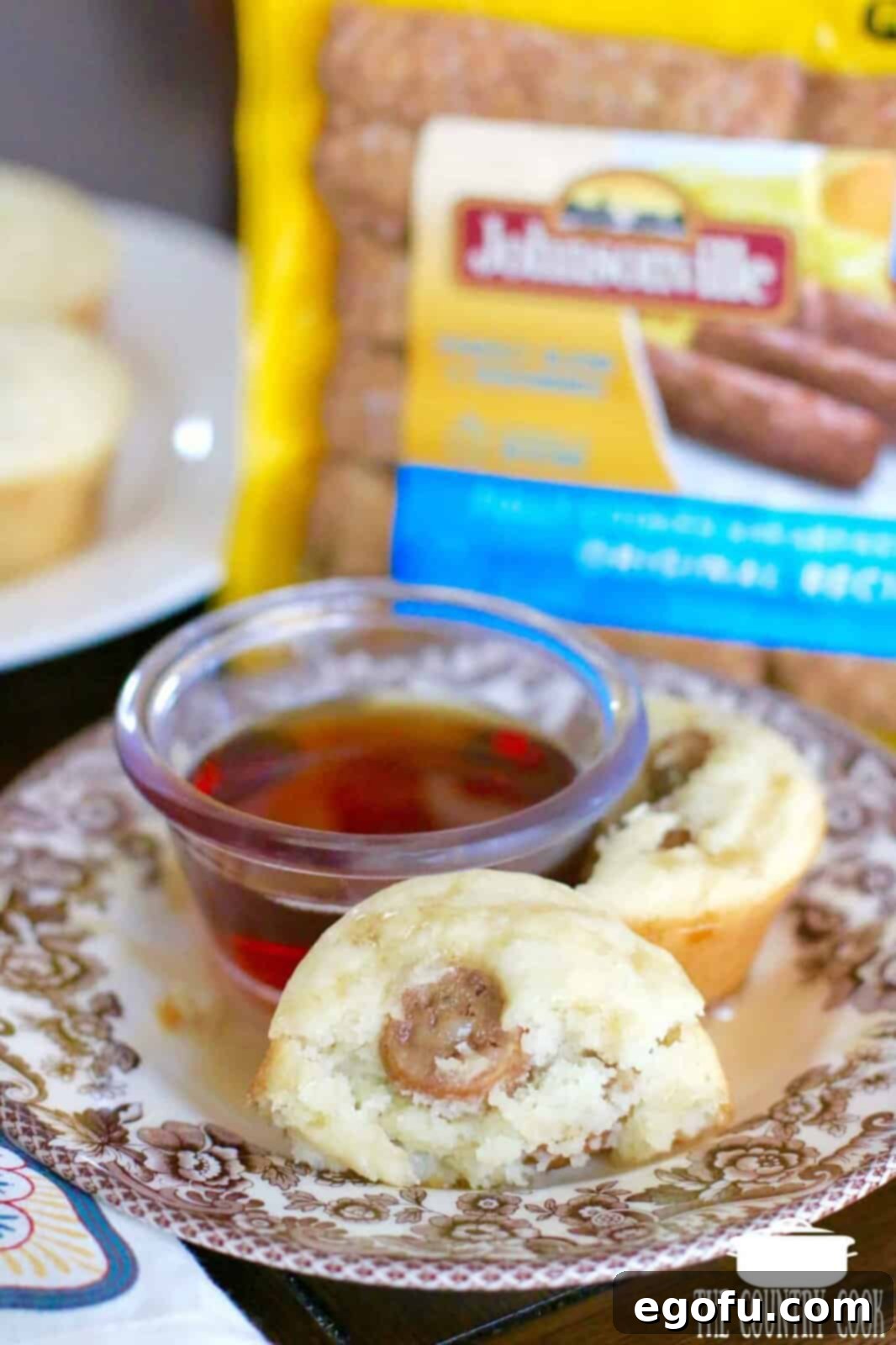 Two golden-brown pancake sausage muffins displayed on a white plate, accompanied by a small bowl of rich maple syrup, ready for a delightful breakfast.