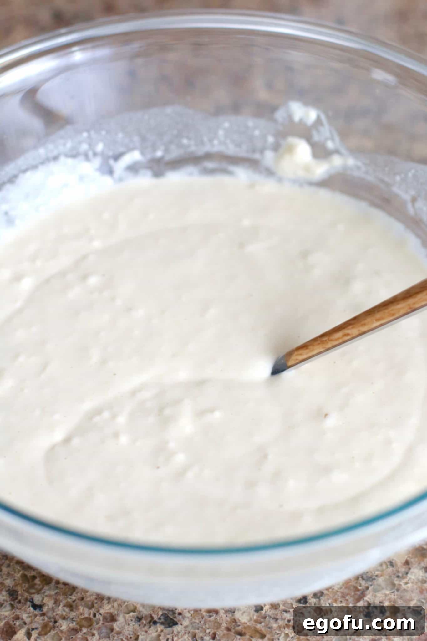Smooth, light yellow pancake batter is visible in a clear mixing bowl, ready for the next step of the recipe.