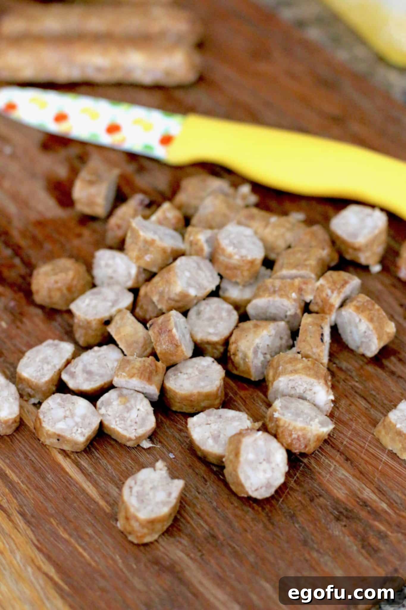 Evenly sliced, cooked breakfast sausages are neatly arranged on a wooden cutting board, prepared for incorporation into the muffin batter.