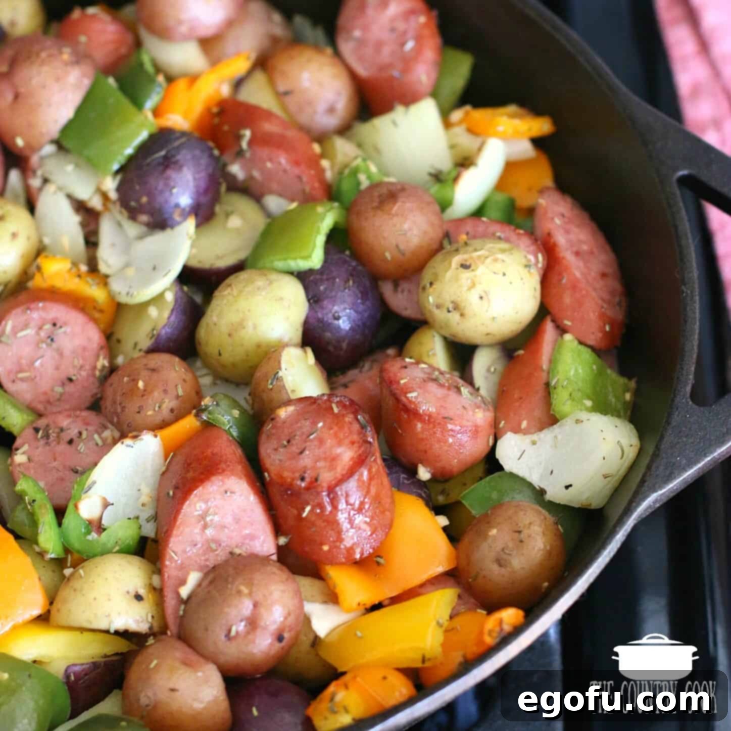 Sliced kielbasa, baby potatoes, peppers and onions shown close up in a cast iron skillet, ready for the oven.