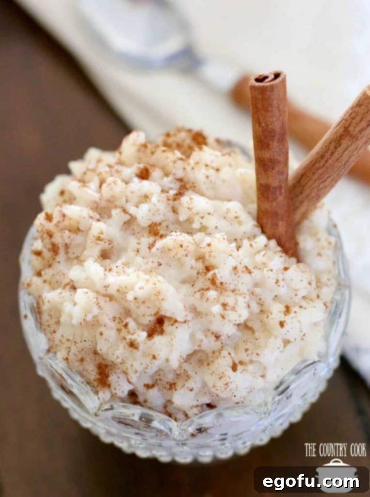 Creamy Crock Pot Rice Pudding 10 rice pudding in a decorative clear glass dessert bowl with two cinnamon sticks.