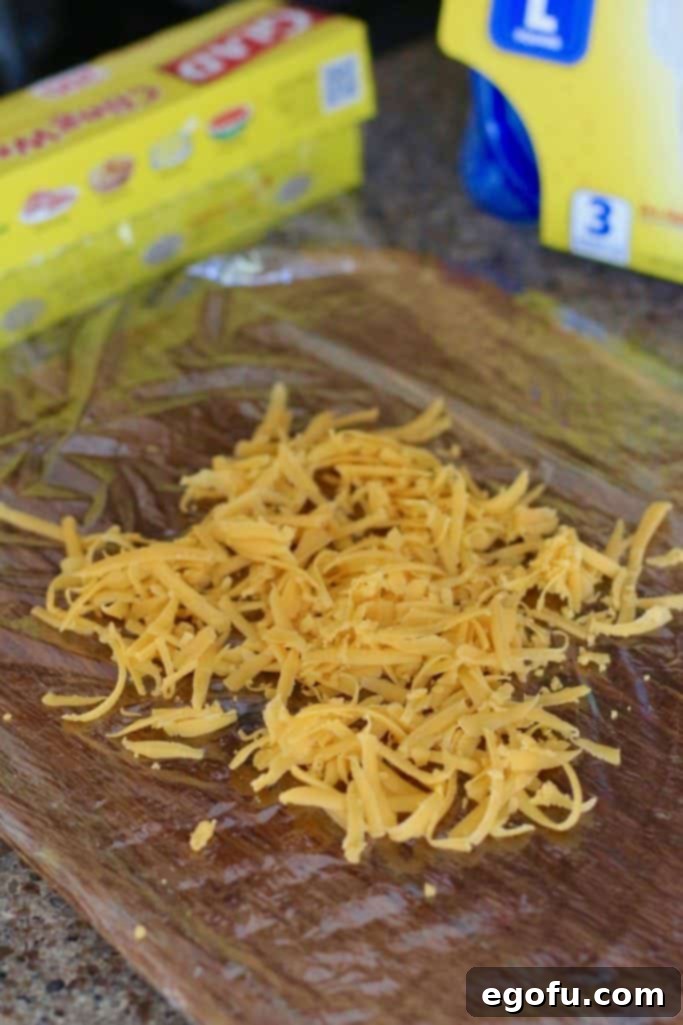 The Great Pumpkin Cheese Ball 12 shredded cheddar cheese placed on top of plastic wrap.