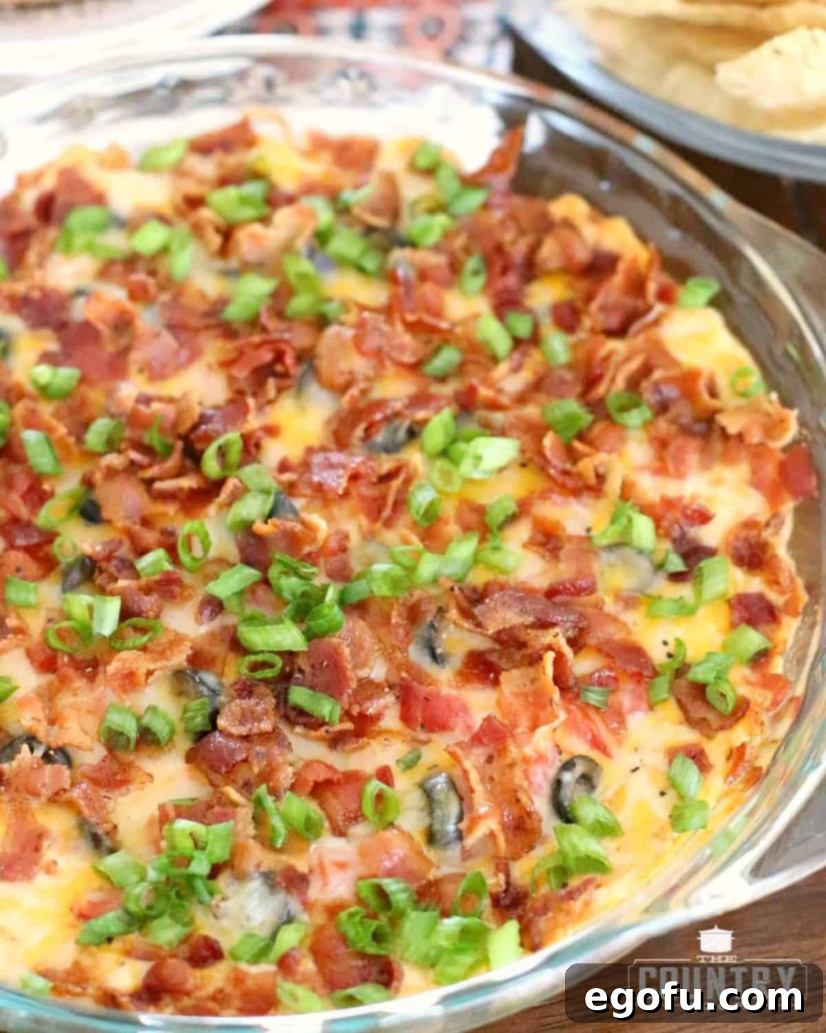 Hot Cheesy Bacon Dip 2 Fully baked Warm Bacon Cheddar Dip in a clear pie baking dish, garnished with fresh green onions.