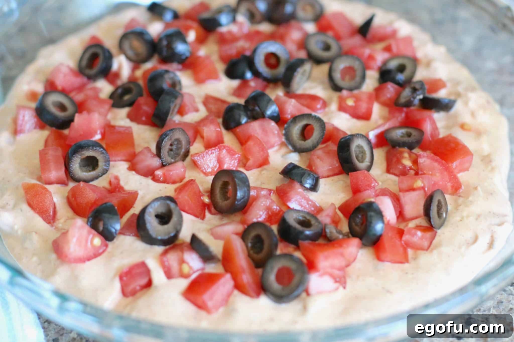 Hot Cheesy Bacon Dip 6 Sliced olives and tomatoes artfully arranged on top of the dip mixture in a round baking dish.