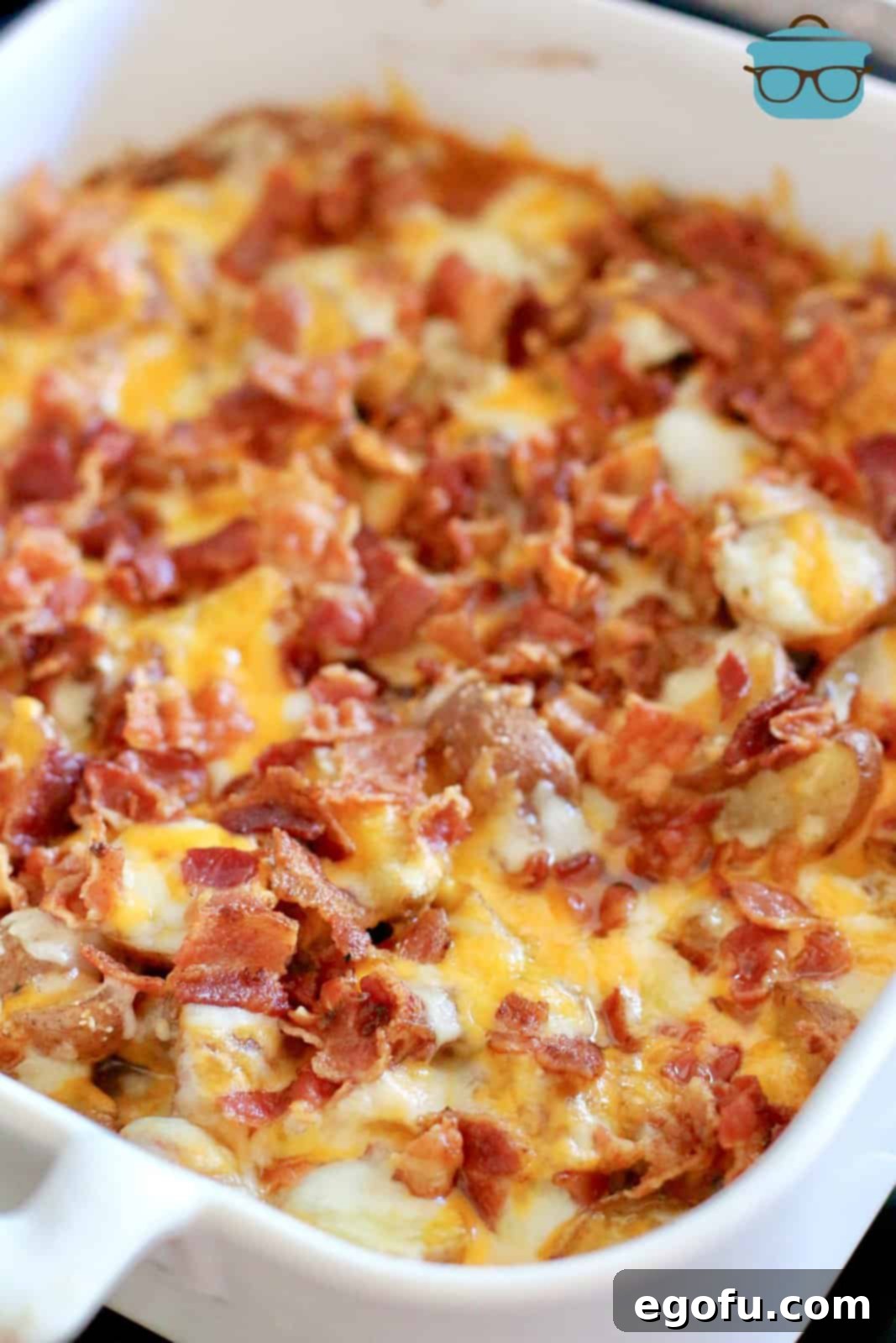 Melted cheese and crumbled bacon shown on cooked potatoes in a white baking dish.