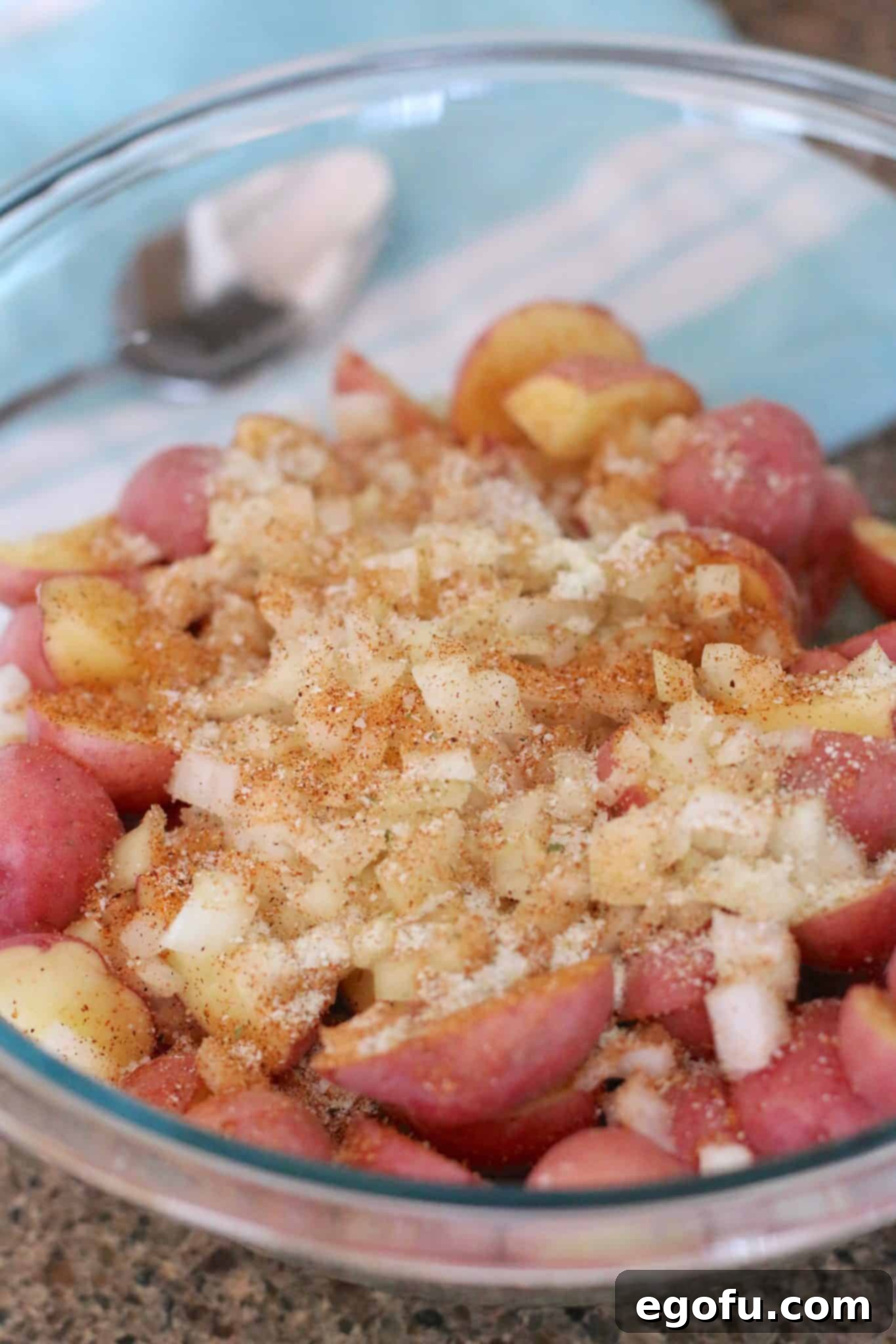 Sliced baby red potatoes, diced onions, seasoned salt, garlic salt in a large clear Pyrex bowl.
