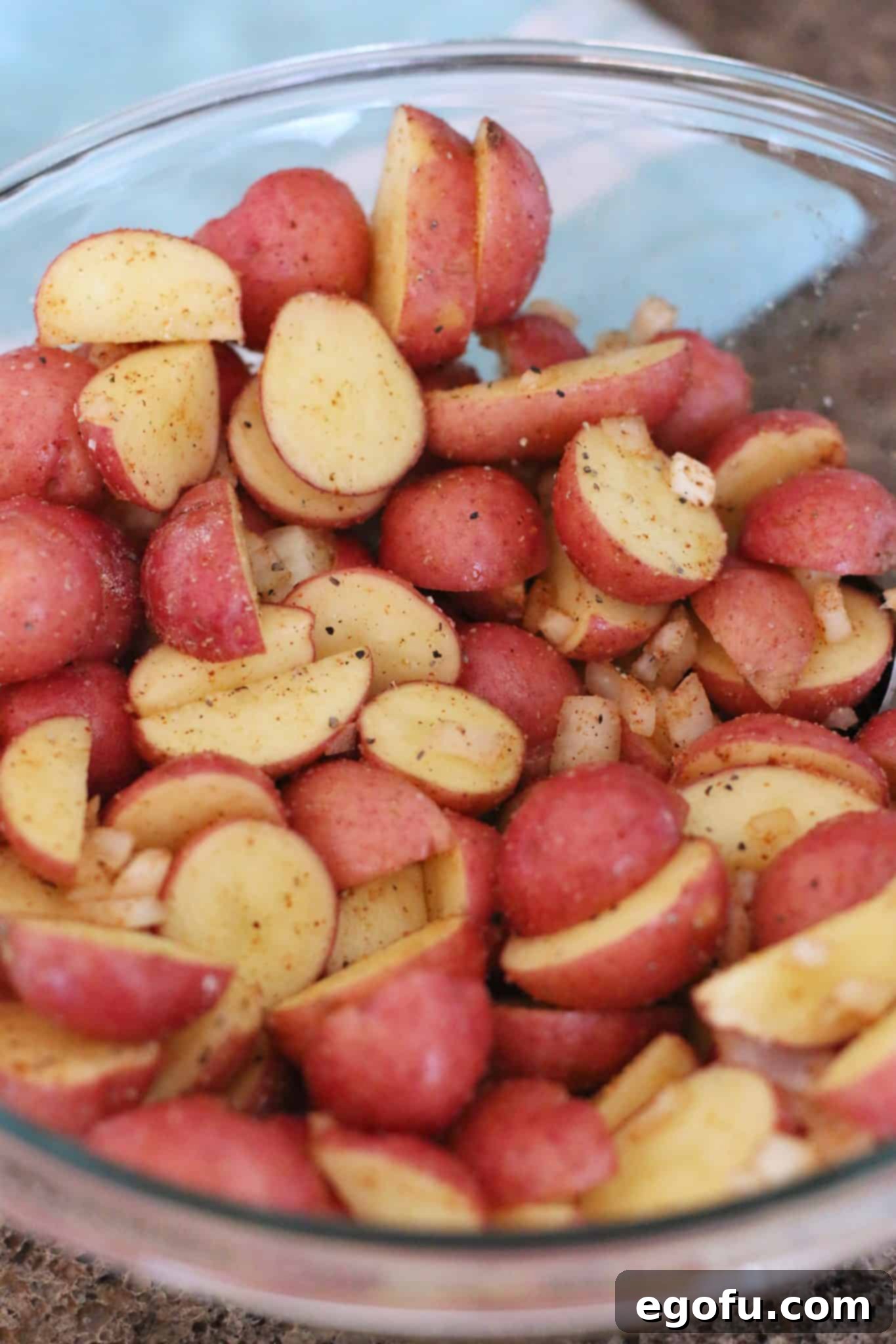 Sliced red potatoes with seasoning stirred together in a bowl.
