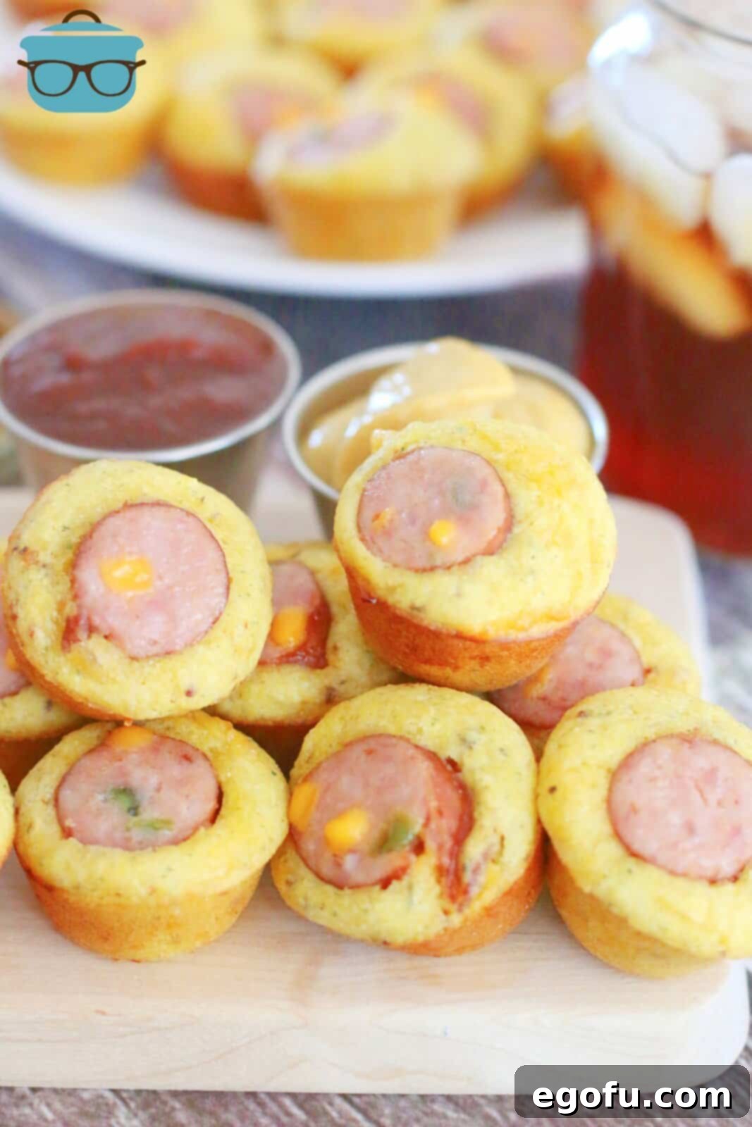 Stack of golden-brown cornbread sausage muffins on a rustic wooden cutting board, garnished with fresh herbs, emphasizing their inviting texture and rich color.